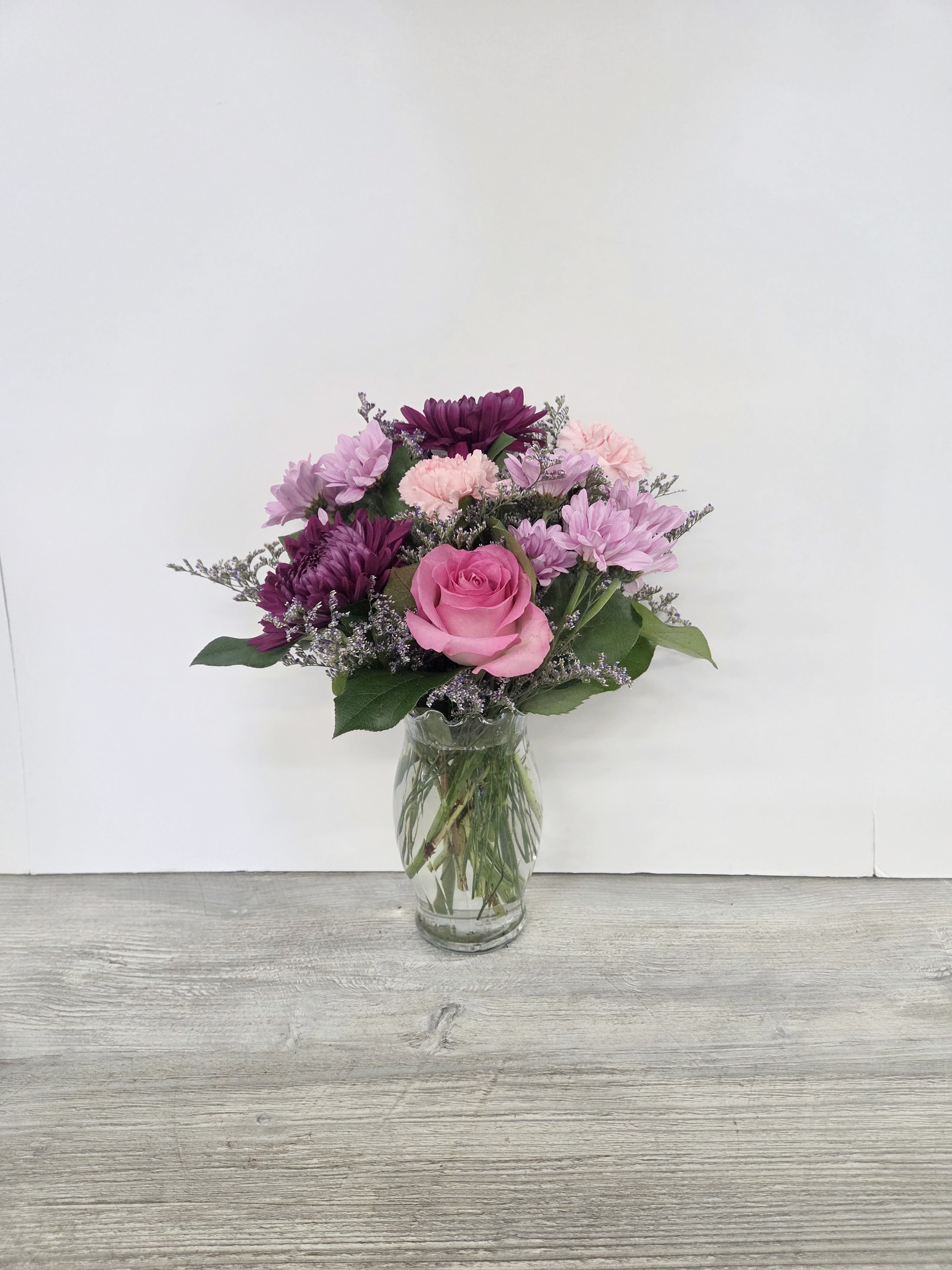 Pink and purple mixed flower arrangement with a rose and mums in a clear glass vase