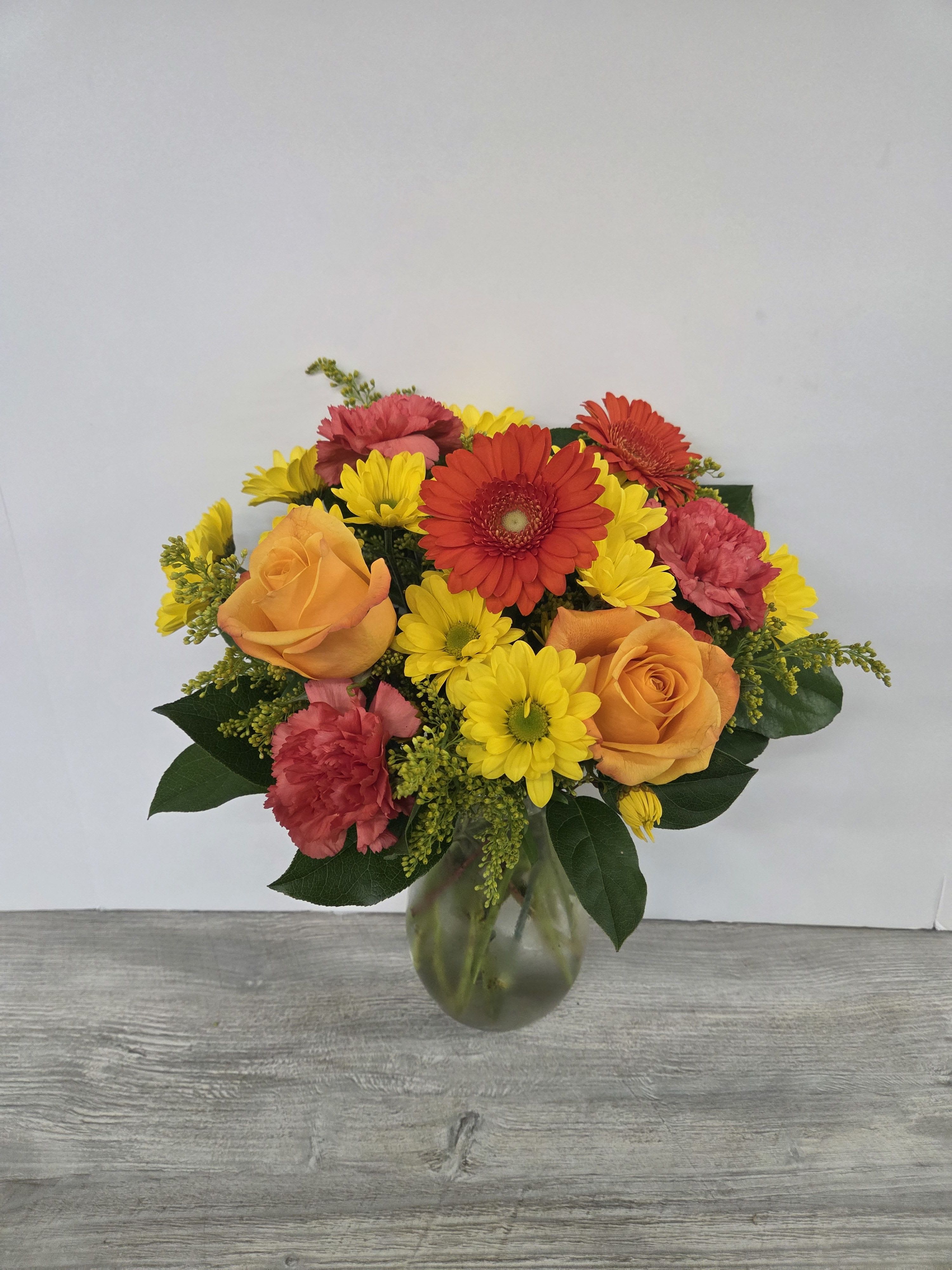 Bright bouquet of orange roses, red gerberas, yellow daisies, and carnations in a glass vase
