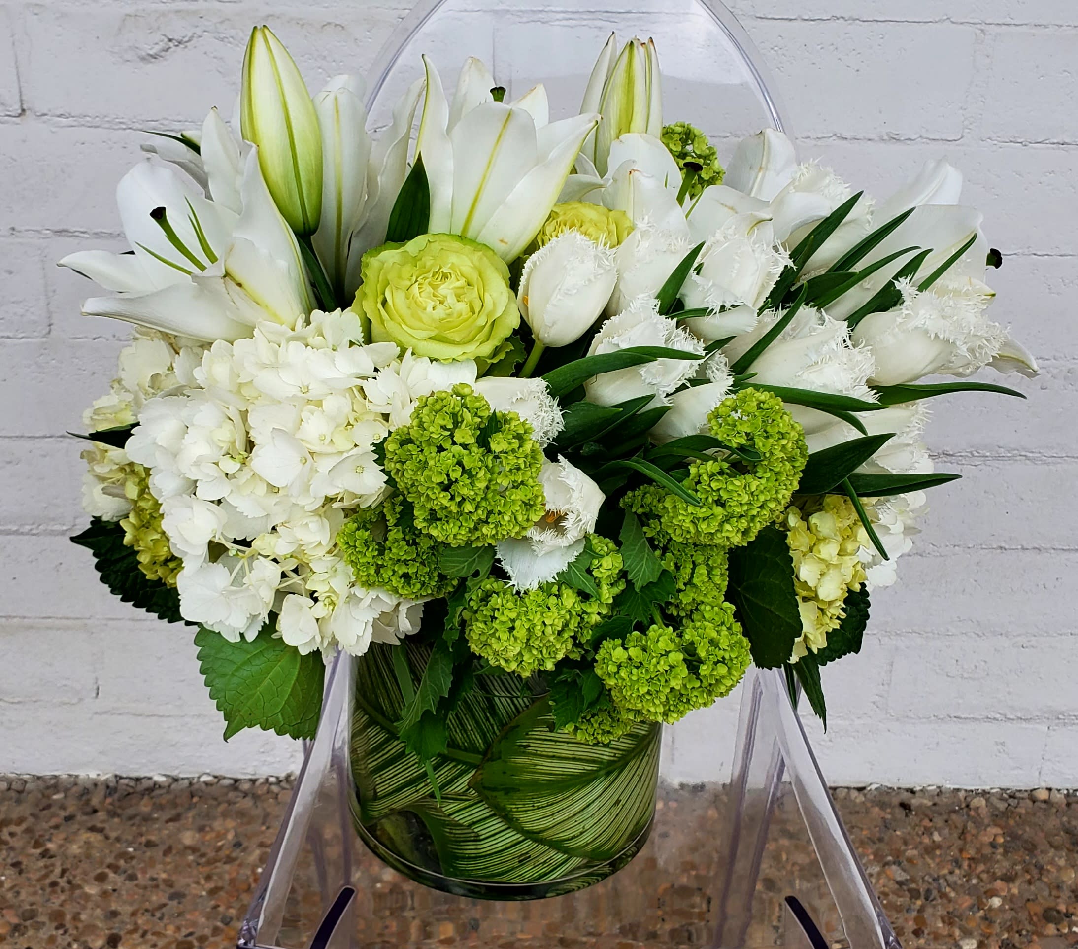 White lilies and green-white blooms arranged in a glass vase