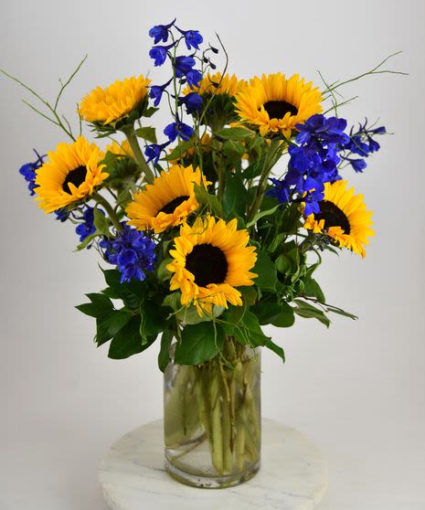Afternoon Delight - Brighten someone’s day with Afternoon Delight, a stunning bouquet designed to capture the warmth and joy of a perfect sunny afternoon. This handcrafted arrangement features vibrant yellow sunflowers paired with striking blue delphiniums, artfully arranged in a clear glass vase. The bold color combination creates an uplifting display that radiates happiness and natural beauty. Perfect for birthdays, thank-you gifts, get-well wishes, or home décor. Each bouquet is freshly arranged by our local florist with care and attention to detail, ensuring long-lasting freshness and beauty. Available for same-day flower delivery in the Omaha Metro area if ordered by 12 Noon for same day delivery   