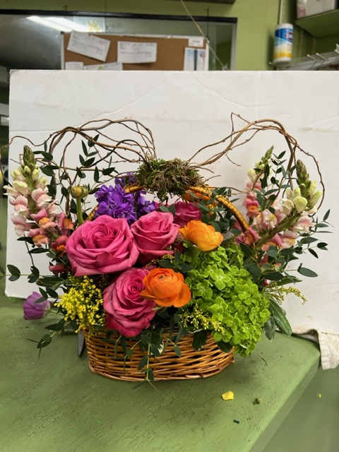 Basket arrangement with pink roses, orange ranunculus, and purple blooms