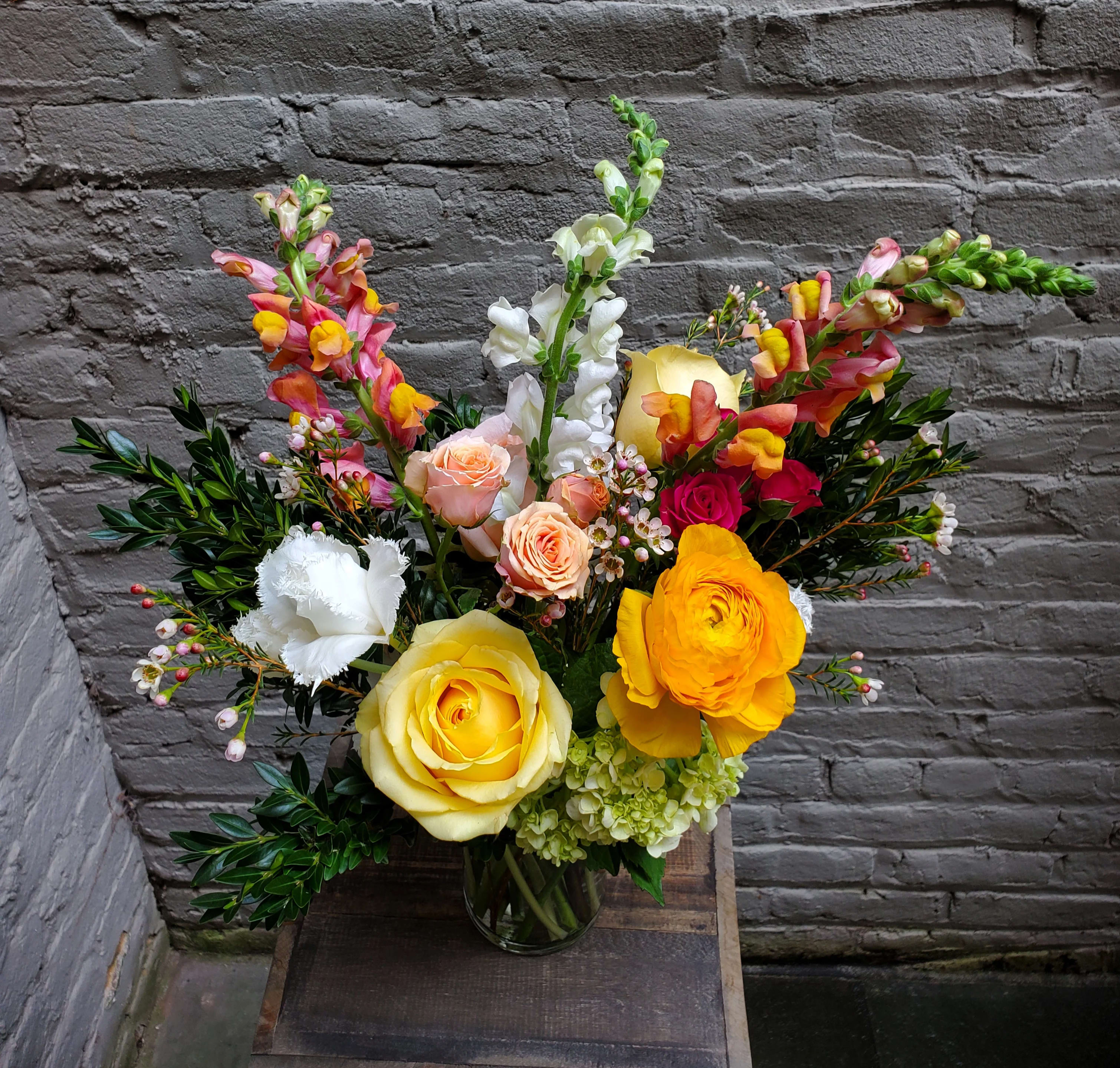 Mixed bouquet of roses, ranunculus, and snapdragons in a glass vase