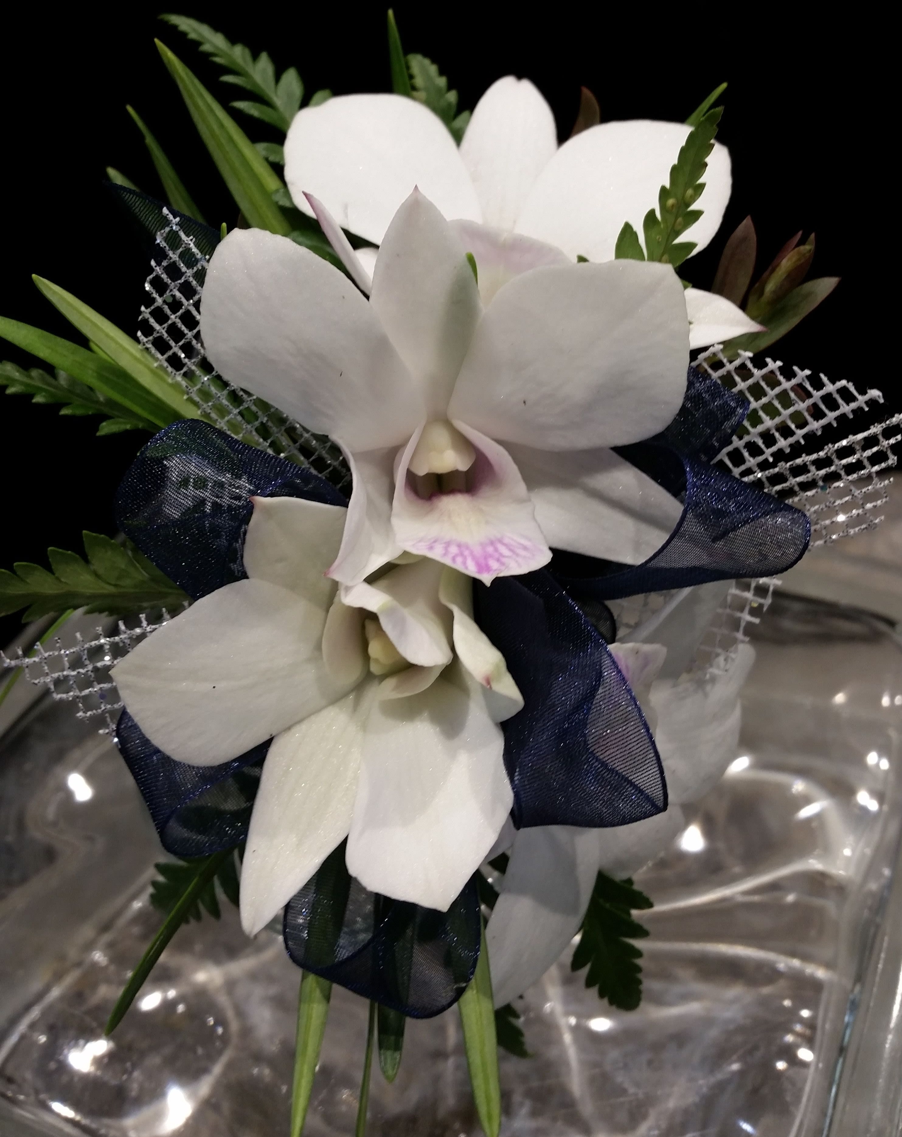 'Dress Blues' White Orchid and Navy Wrist Corsage - This elegant wristlet is first class!  The best white dendrobium orchids with a hint of lavender, sheer navy ribbon and a touch of glitz make this one of our favorites!   PLEASE CALL THE SHOP AT (617)244-4422 ALL CORSAGE OR BOUTONNIERE ORDERS. THANK YOU.