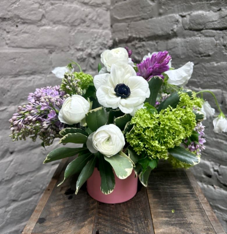 Compact arrangement of white anemones and ranunculus with purple blooms in a pink vase