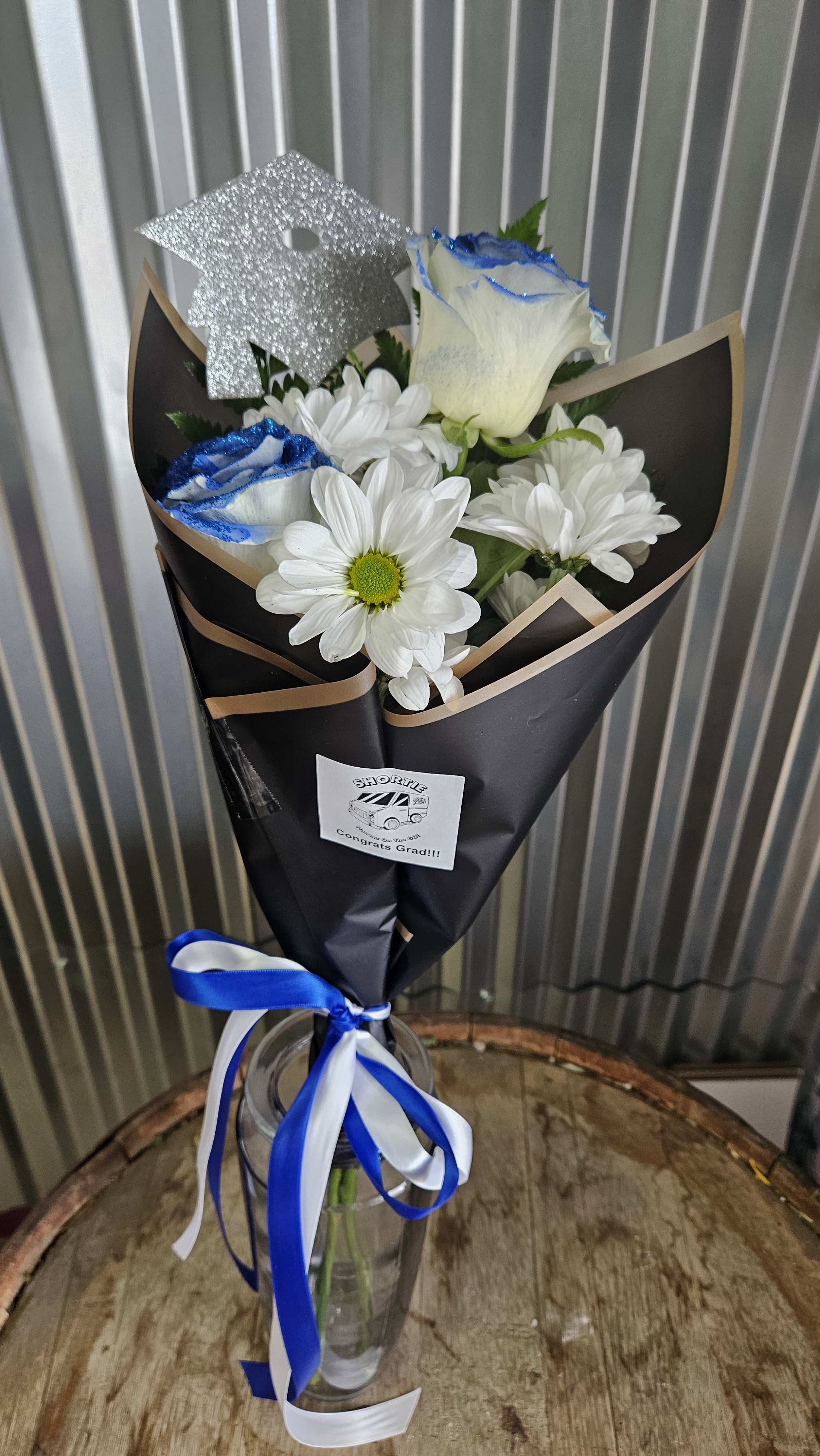 Hand Tied Grad Bouquet In Blue and white - Great way to show your Grad you are proud of them. This has 2 roses, mums and a Grad pick Hand tied with decorative paper and Satin ribbon in school colors 