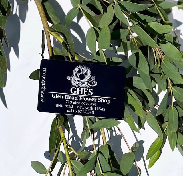 Black Glen Head Flower Shop card resting on long green branches against a white background