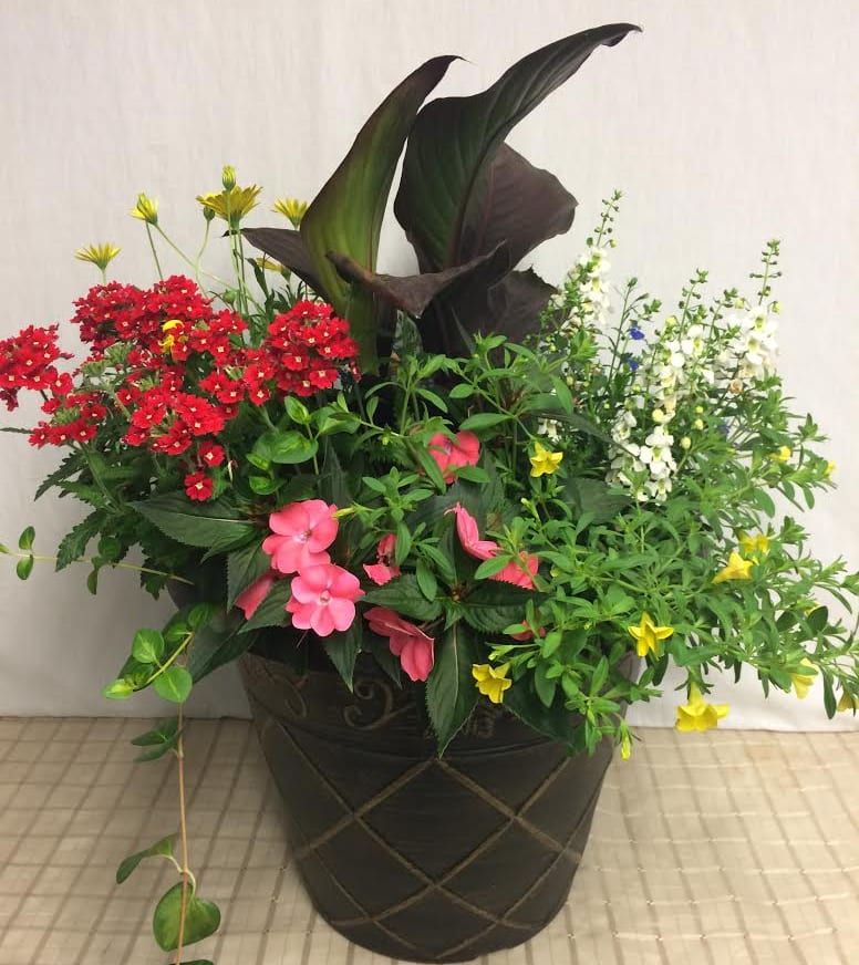 Mixed floral arrangement in a dark decorative pot with red, pink, white, and yellow blooms