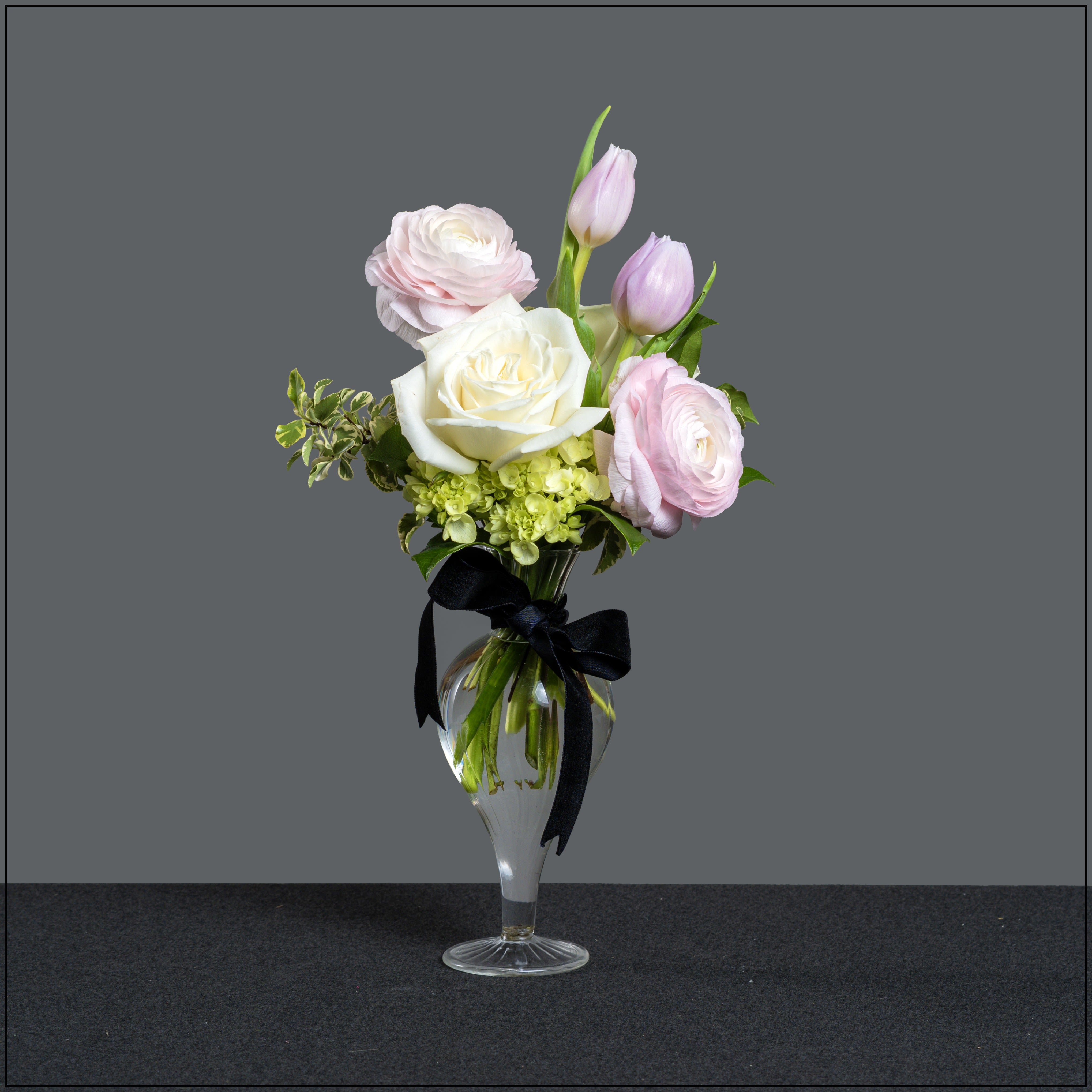 Pink and white flowers arranged in a clear glass vase with a black ribbon