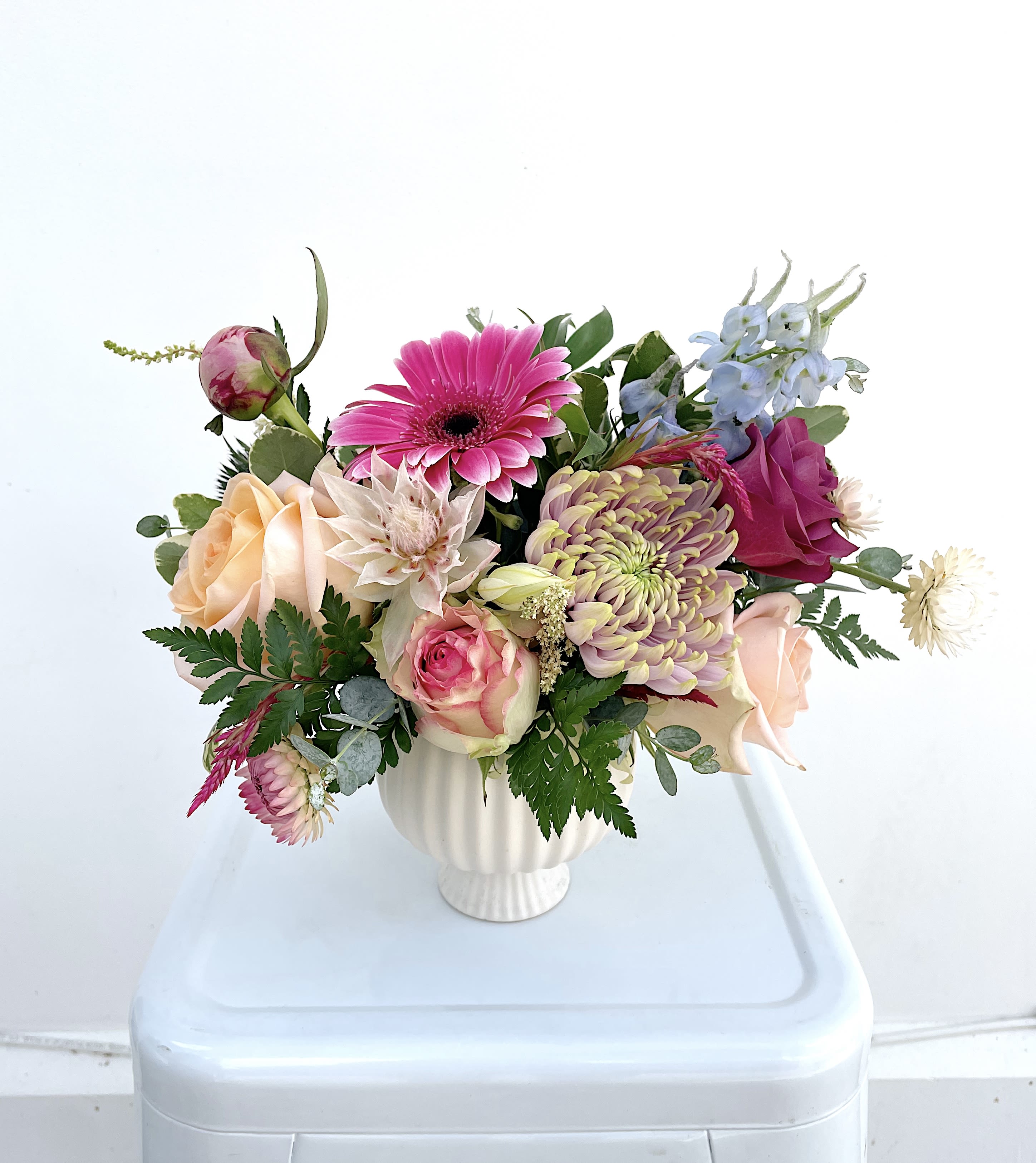 Mixed bouquet in a white vase with pink, peach, and blue flowers