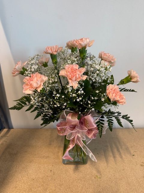 Pink carnations in a glass vase with baby's breath and a pink ribbon
