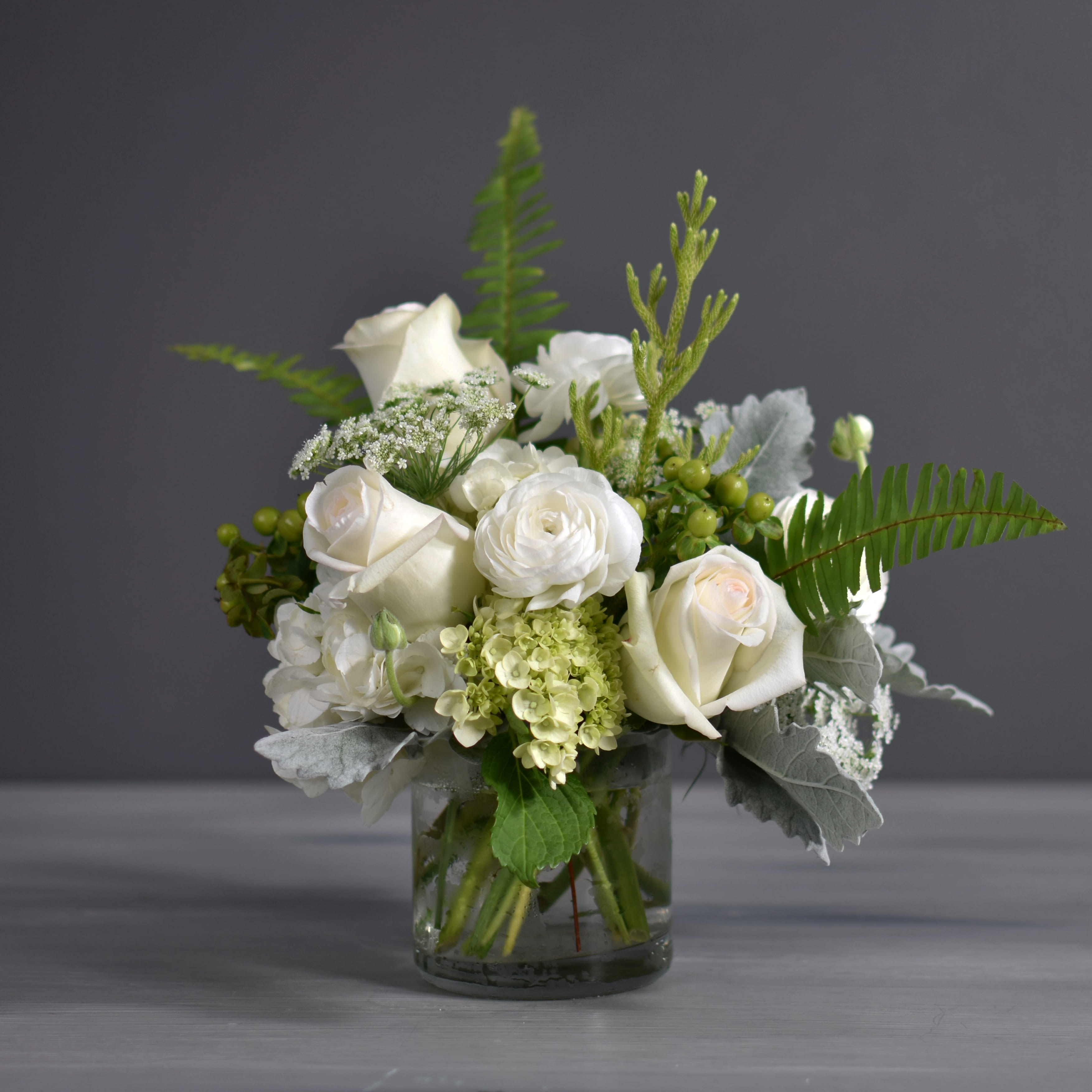 Marlo - White and green hydrangeas, white roses, ranunculus, green hypericum, dusty miller and queen annes lace arranged in an elegant glass cylinder.   Approximately 11 H x 10 W