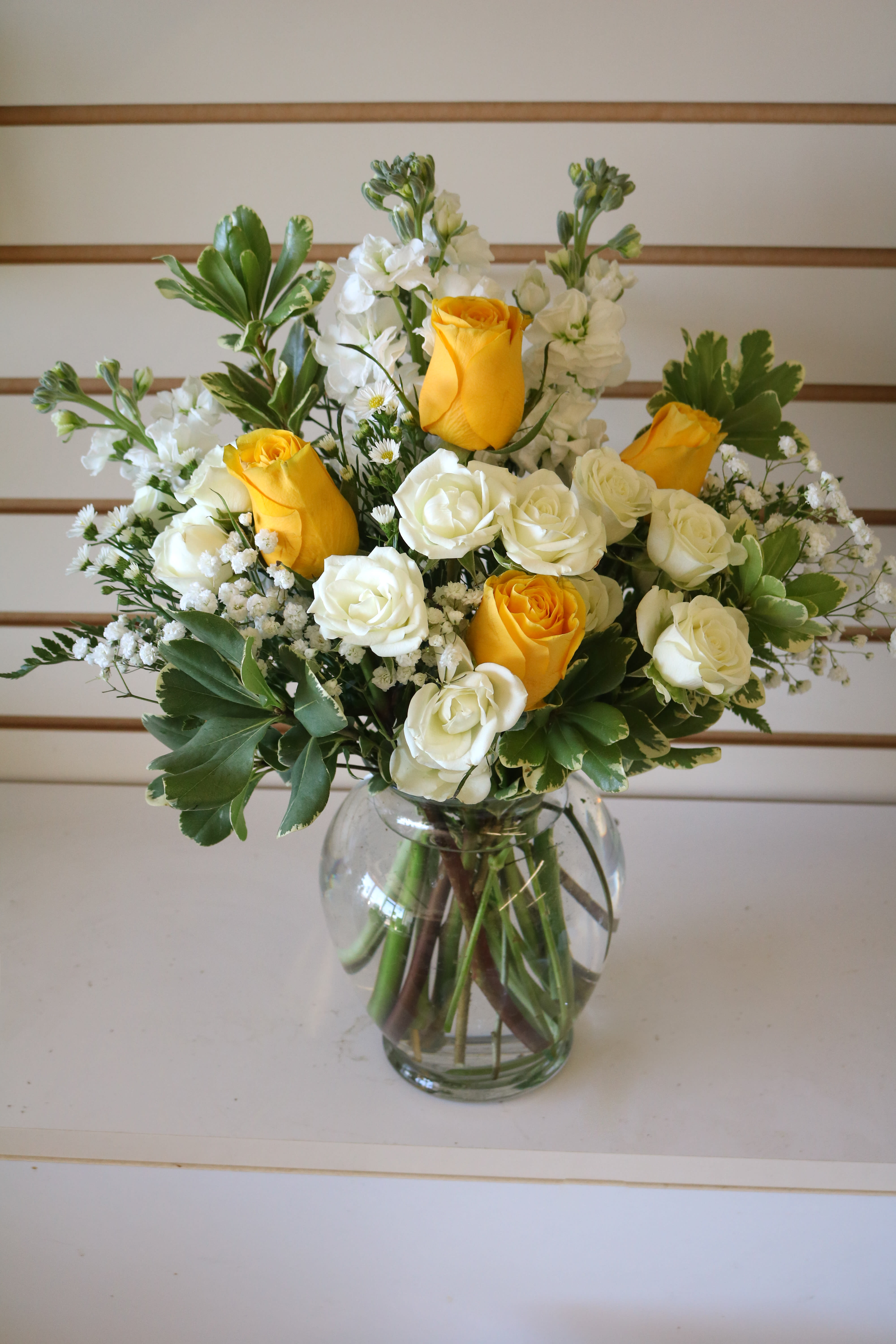 Yellow and white roses arranged in a clear glass vase