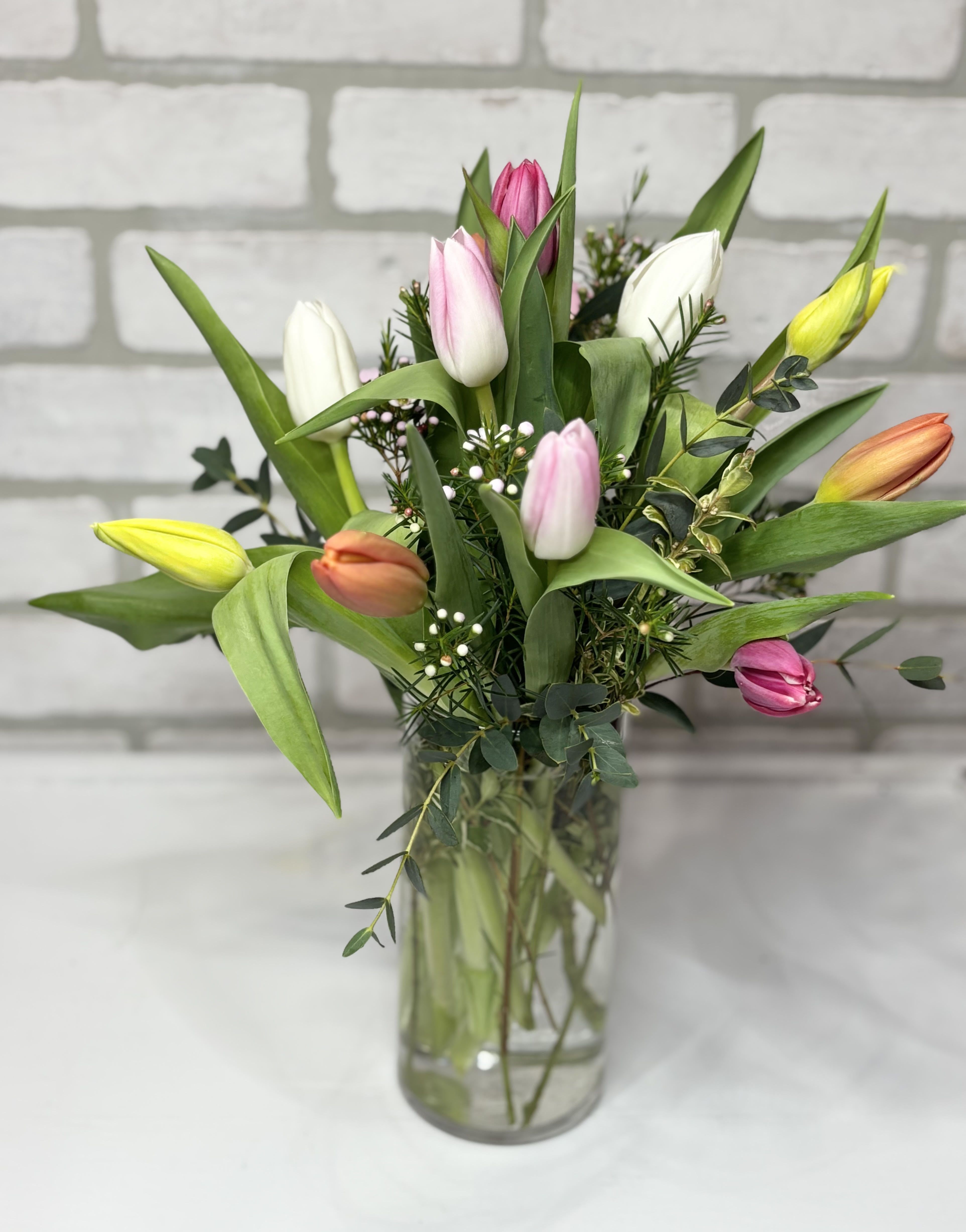 Tall clear vase of mixed pink, white, yellow, and orange tulips with filler flowers
