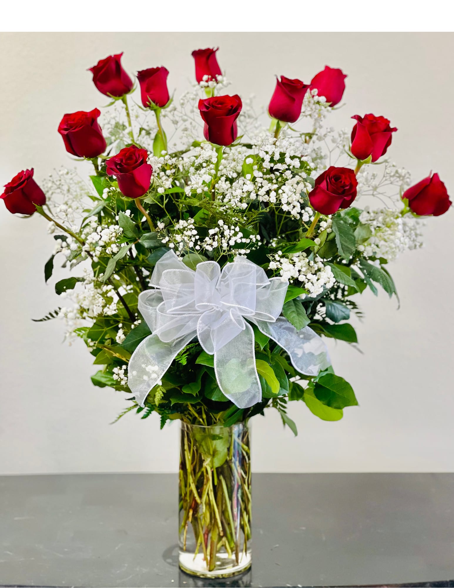 Red roses with white baby's breath in a clear glass vase and white bow