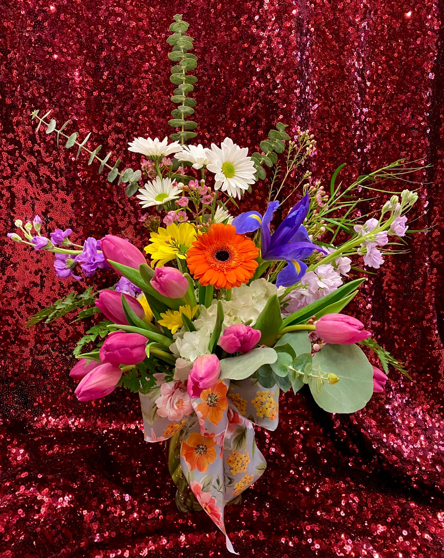 Bright mixed bouquet with pink tulips, daisies, iris and gerbera in a glass vase with a floral bow.