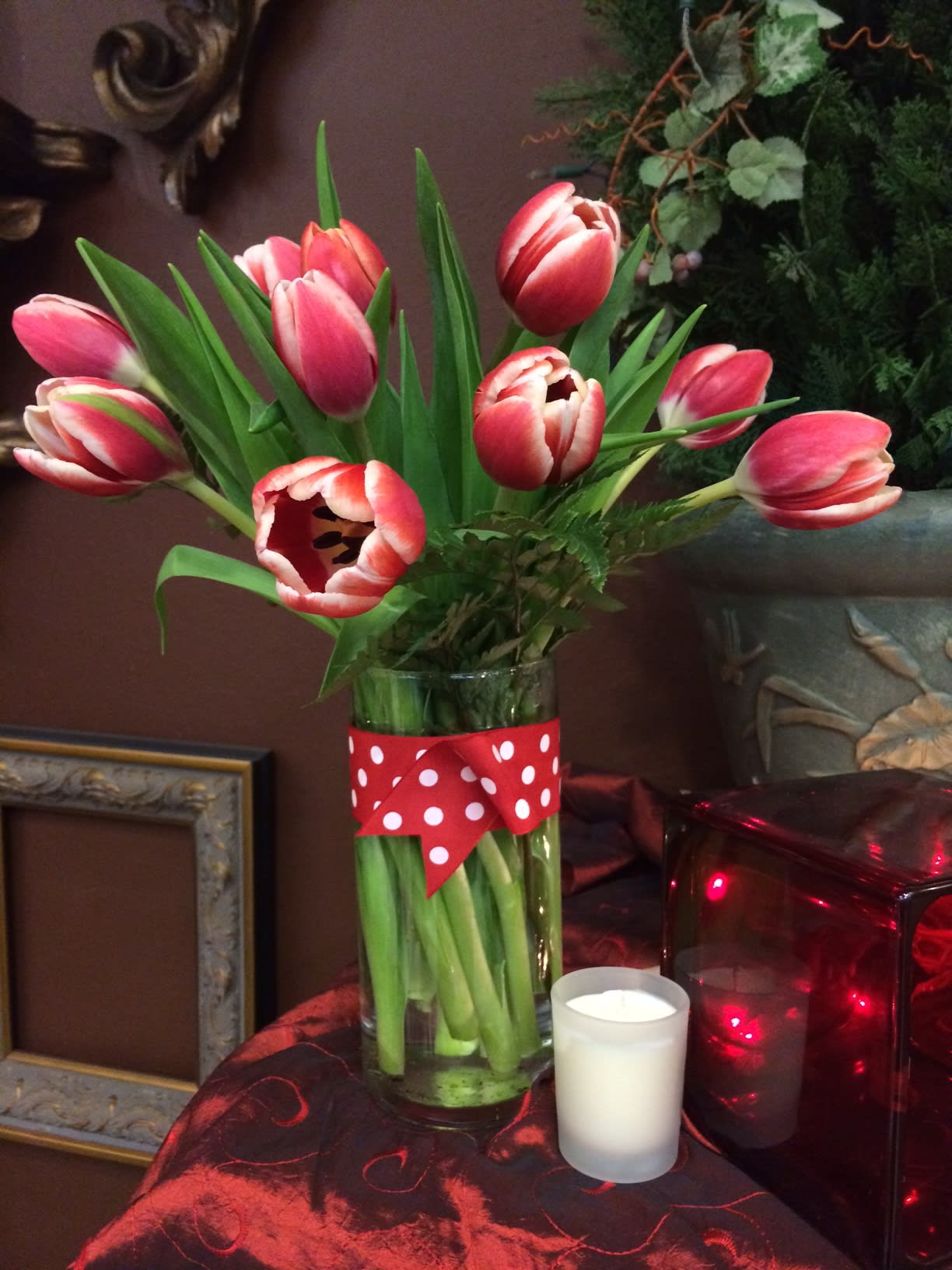 Red and white tulips in a clear vase with polka dot ribbon, next to a small white votive candle.