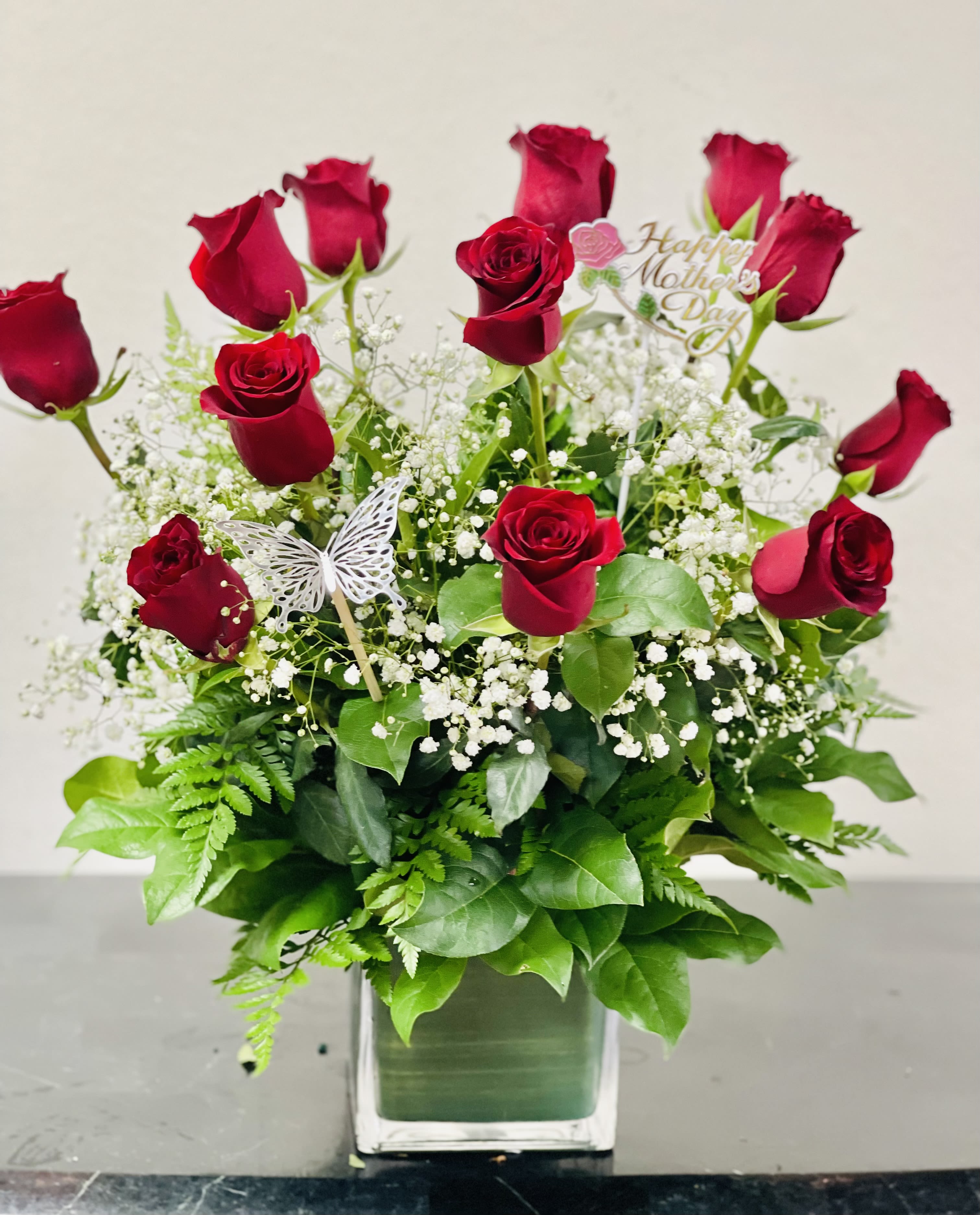 Red roses arranged in a clear square vase with baby's breath and greenery