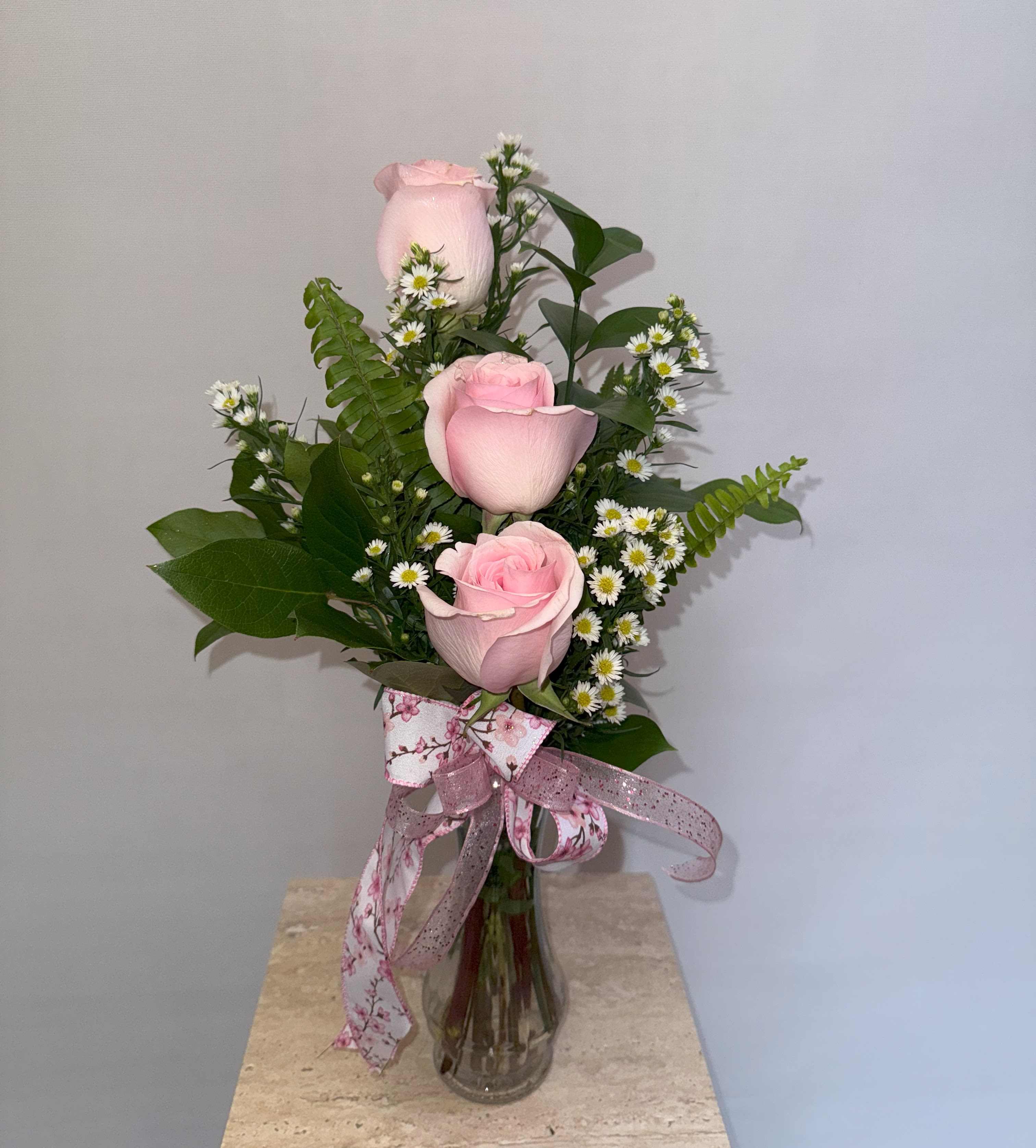 Pink roses arranged in a clear glass vase with small white daisies