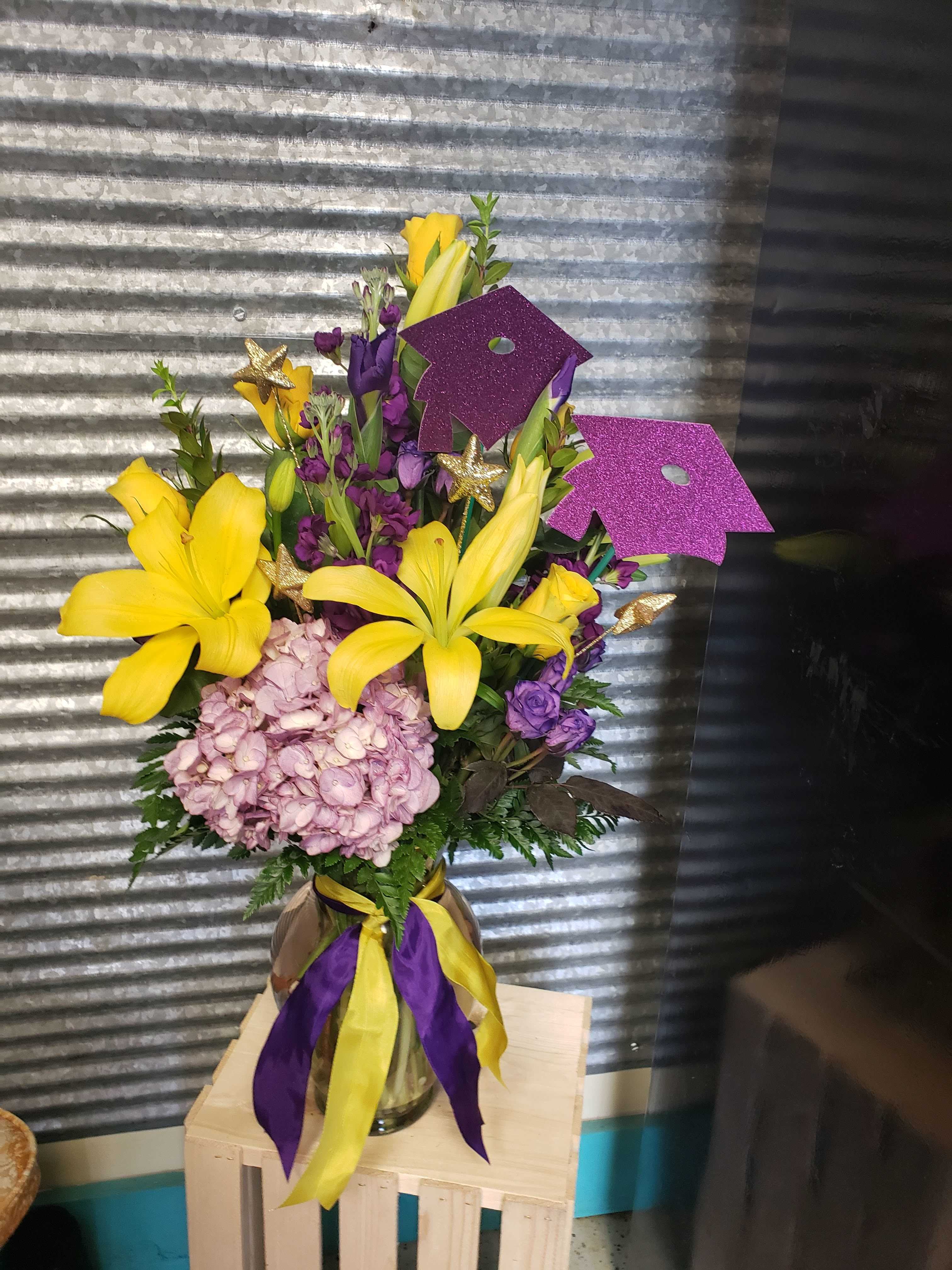 Yellow lilies and purple flowers in a glass vase with ribbon and glitter toppers