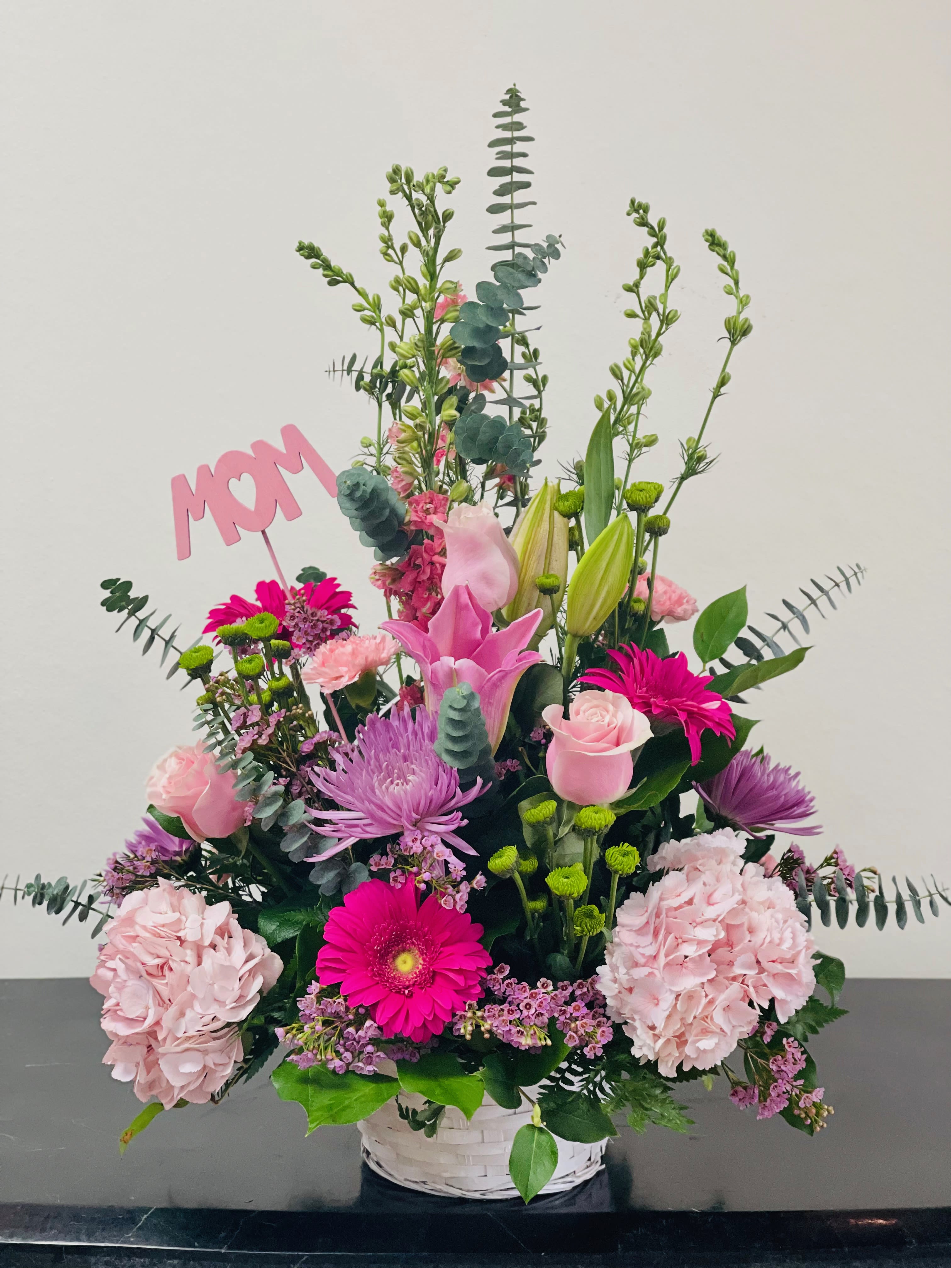 Pink and purple mixed flower arrangement in a white basket with a MOM sign