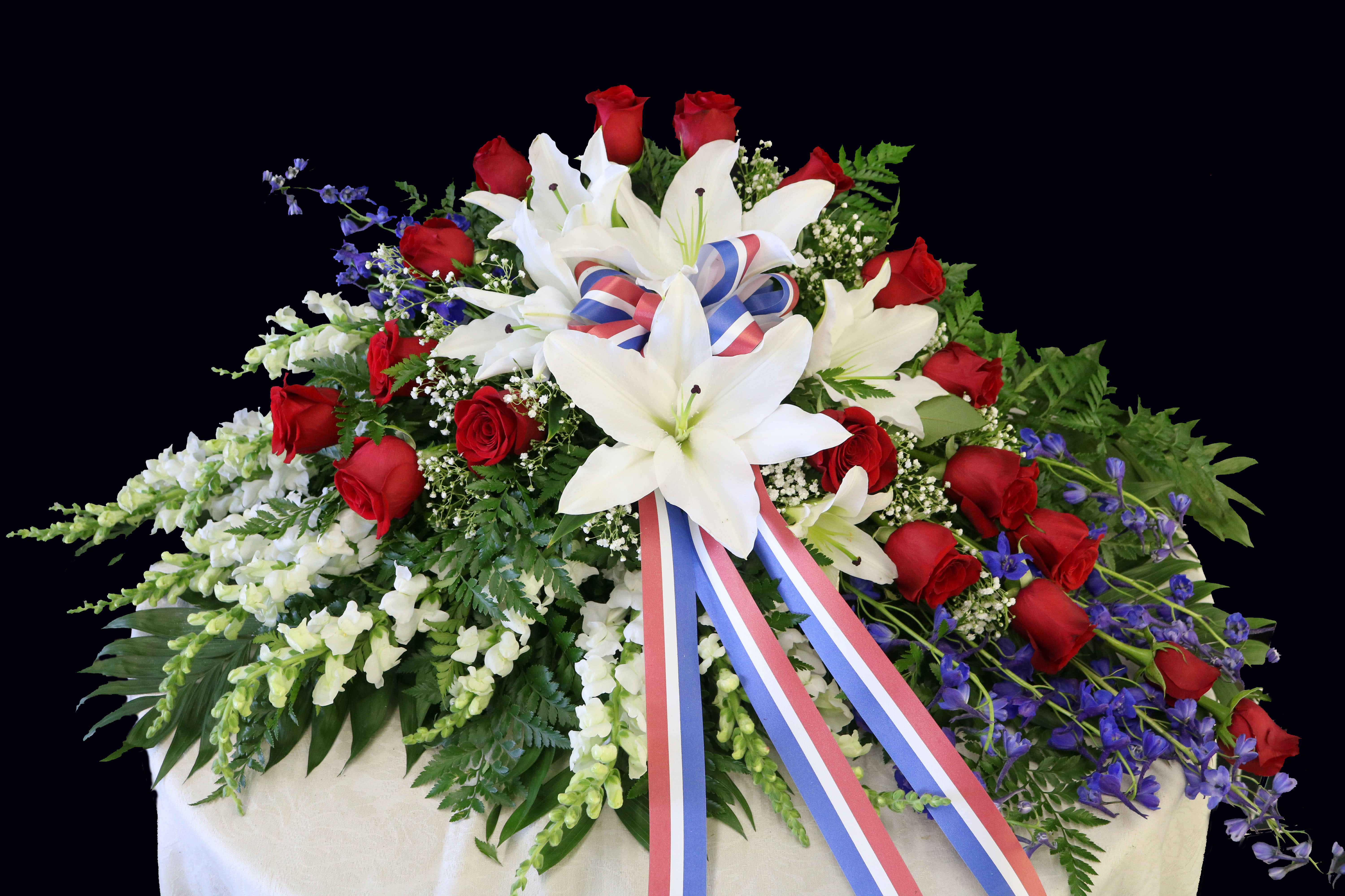 Large funeral spray of red roses and white lilies with a tricolor ribbon