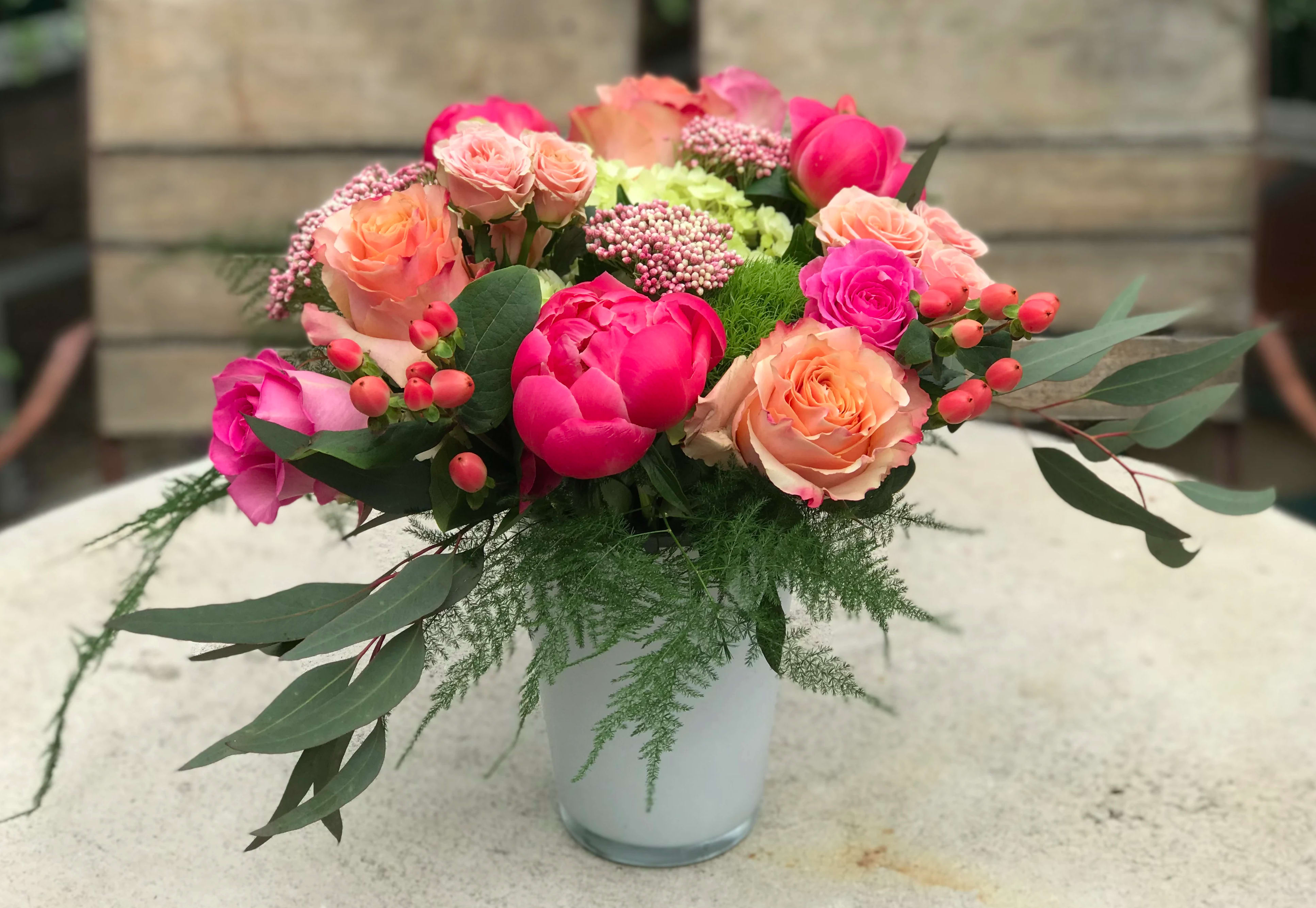 Mixed pink and peach roses in a white vase with greenery