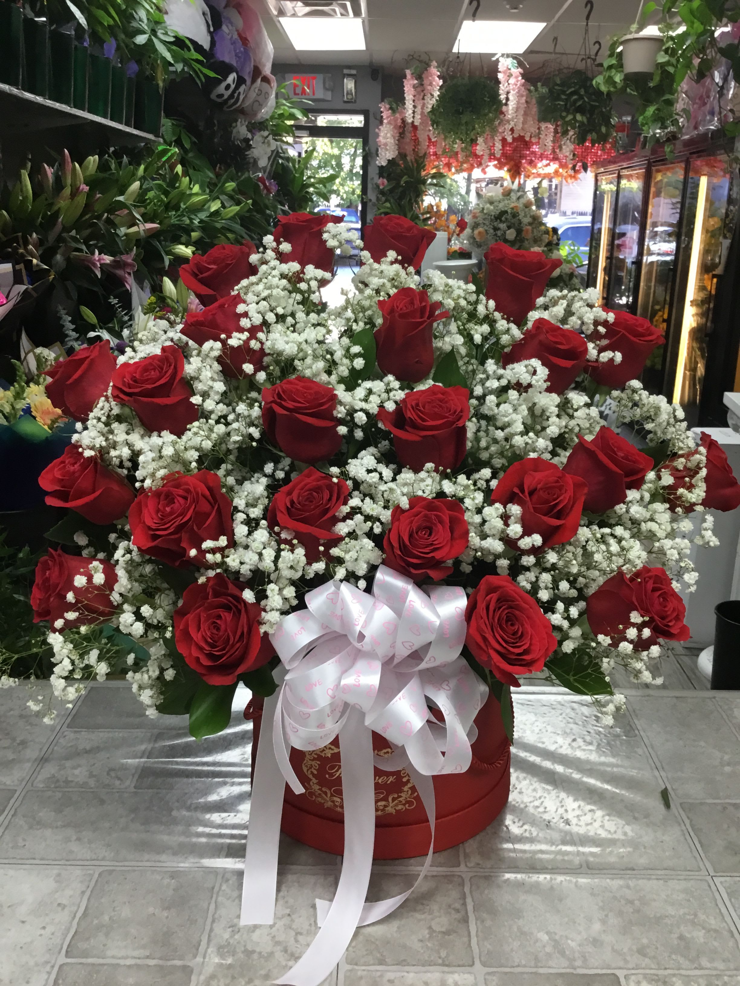 Large red rose arrangement with baby's breath in a round box and white ribbon