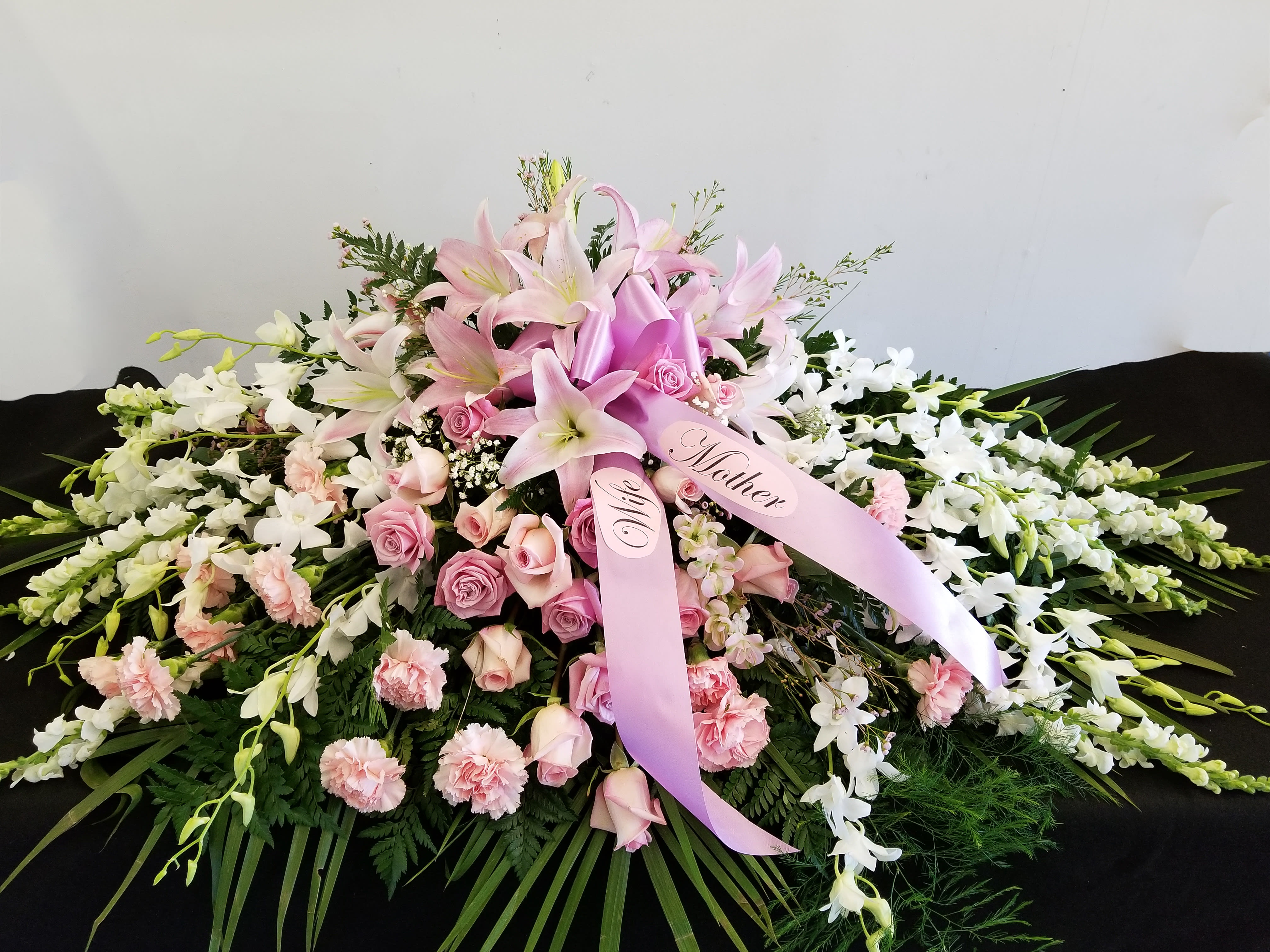 Pink lilies and roses arranged with white orchids and ribbons