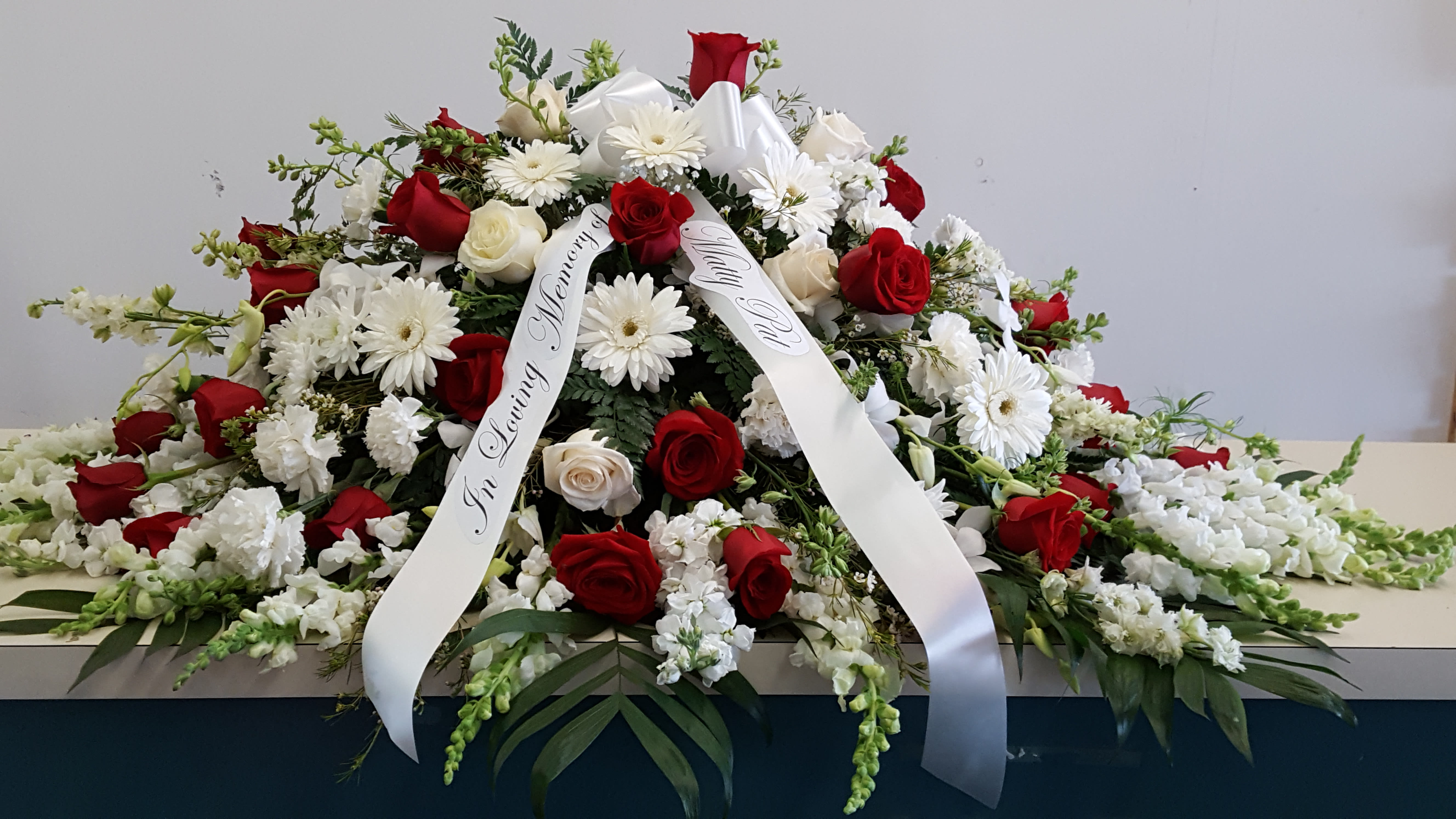 Casket spray of red and white roses with white daisies and ribbon