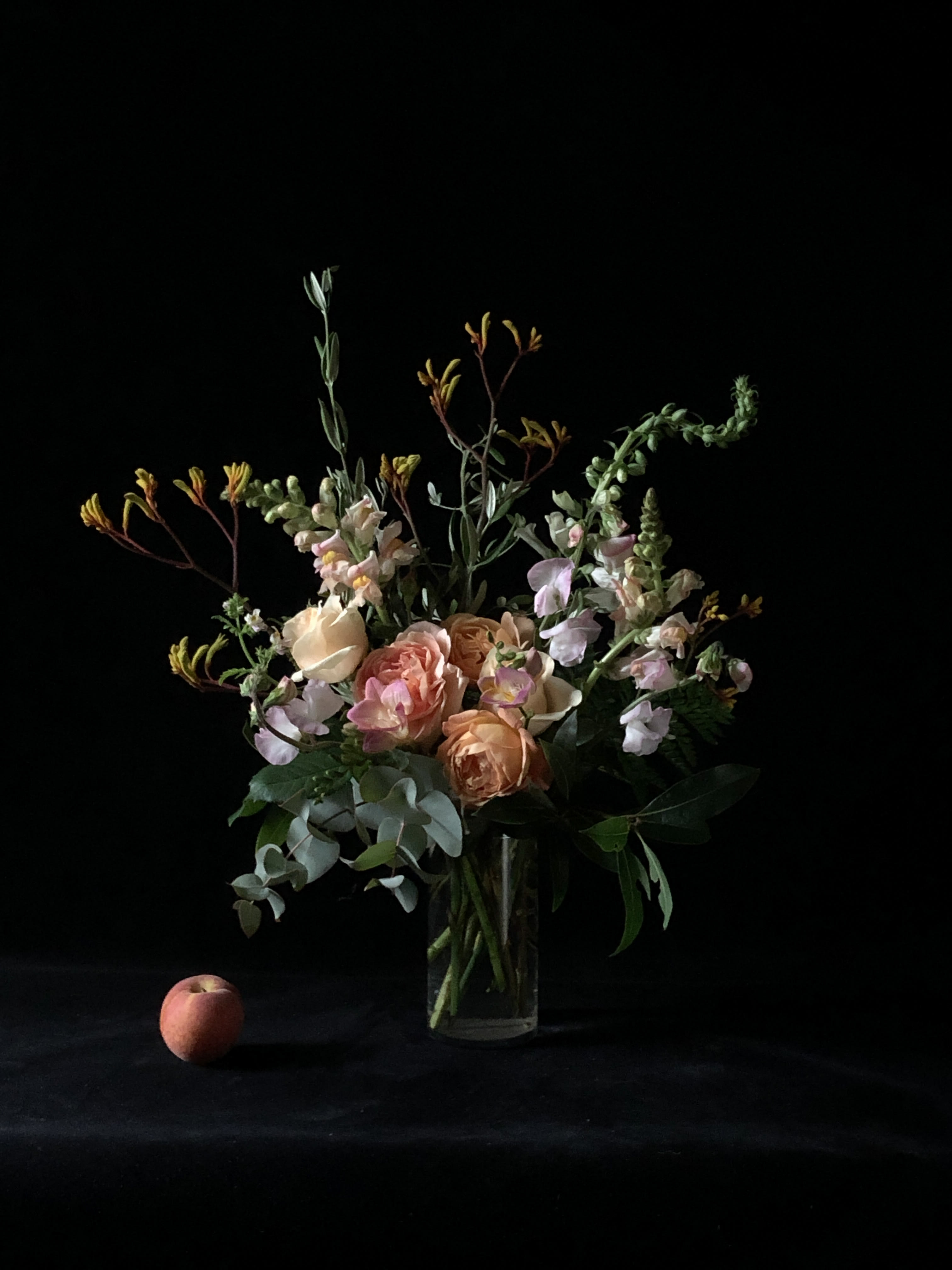 Peach and blush roses in a clear glass vase with airy greenery