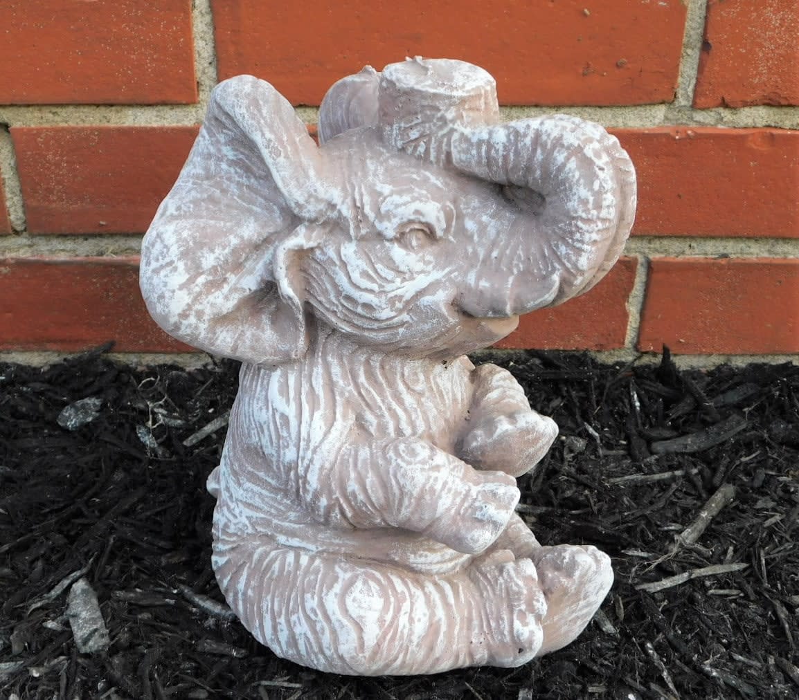 Small elephant figurine in a garden bed against a brick wall