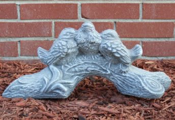 Decorative stone bird sculpture on mulch in front of a brick wall