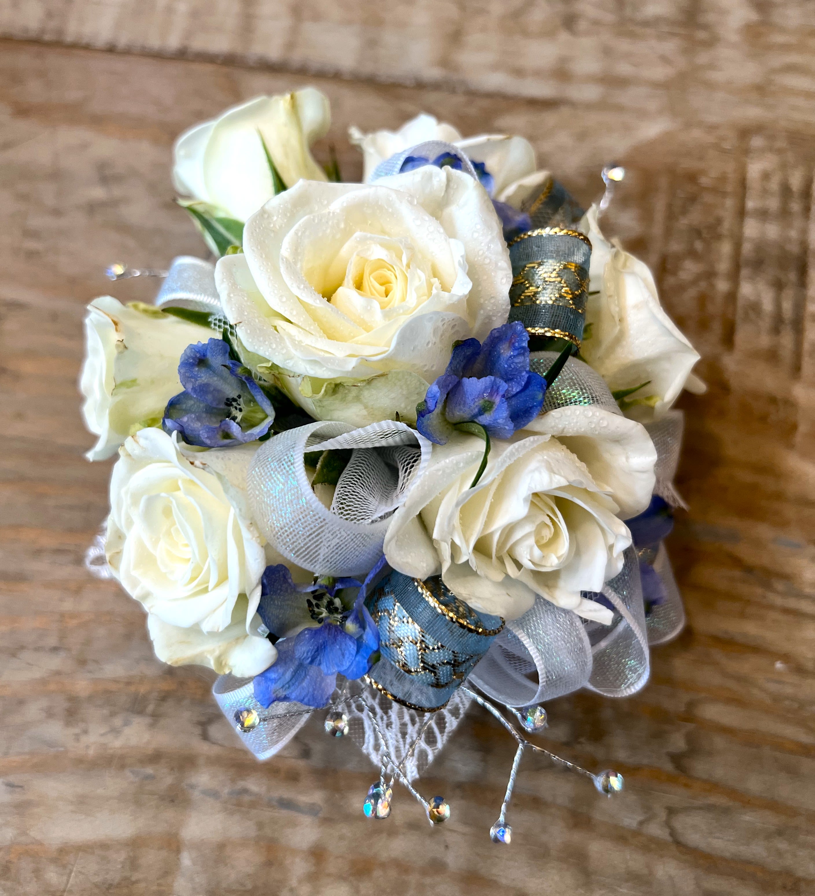 Small corsage of white roses and blue flowers with silver and blue ribbon accents