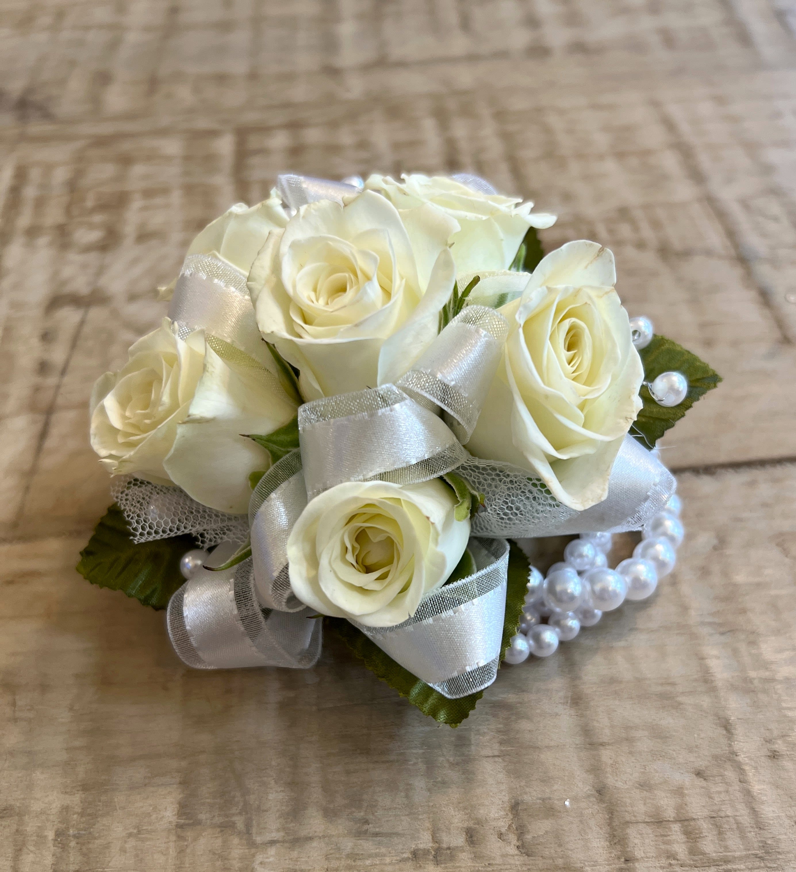 Wrist corsage of ivory spray roses with silver ribbon and a pearl bracelet band
