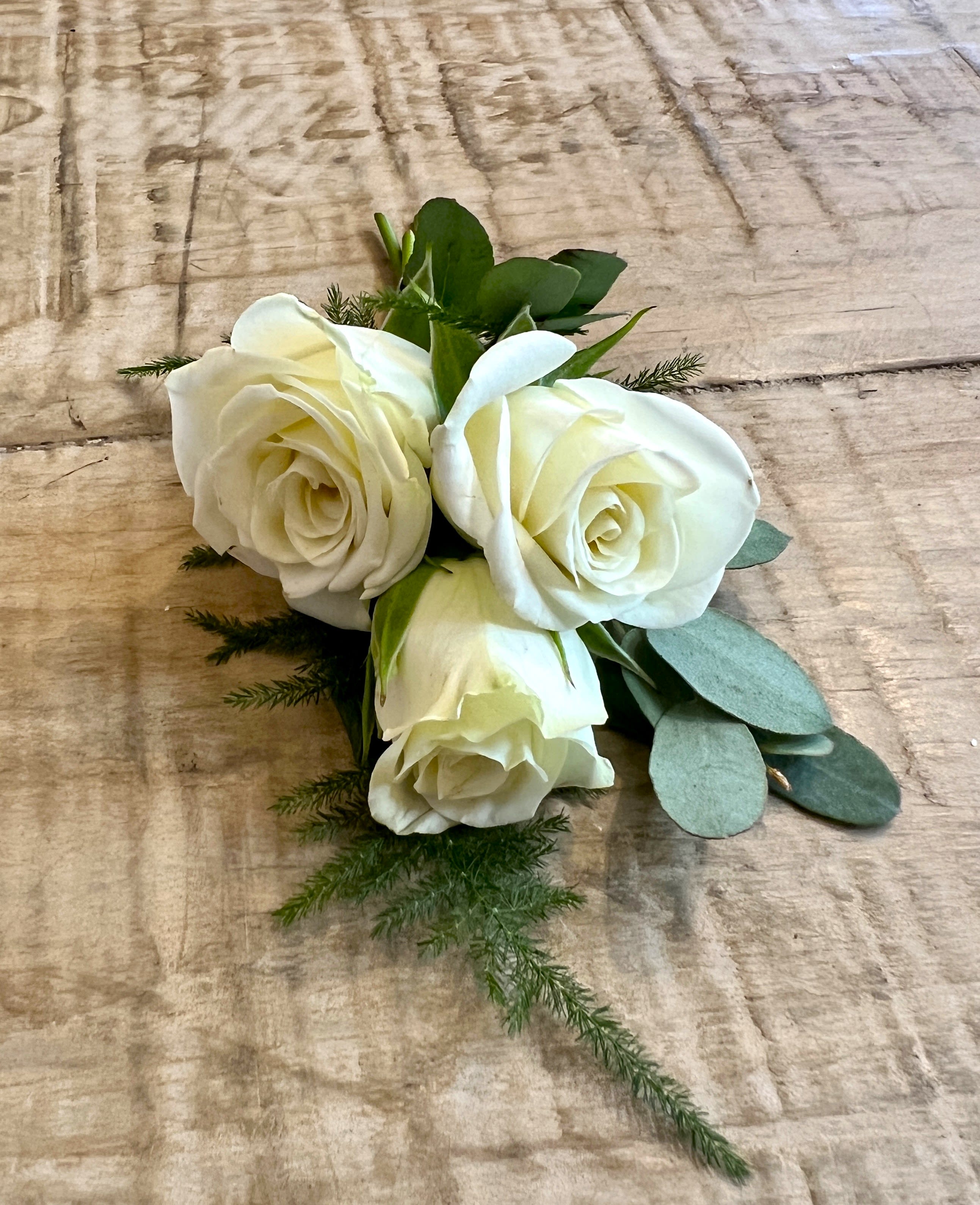 Three white roses with greenery on a wooden surface