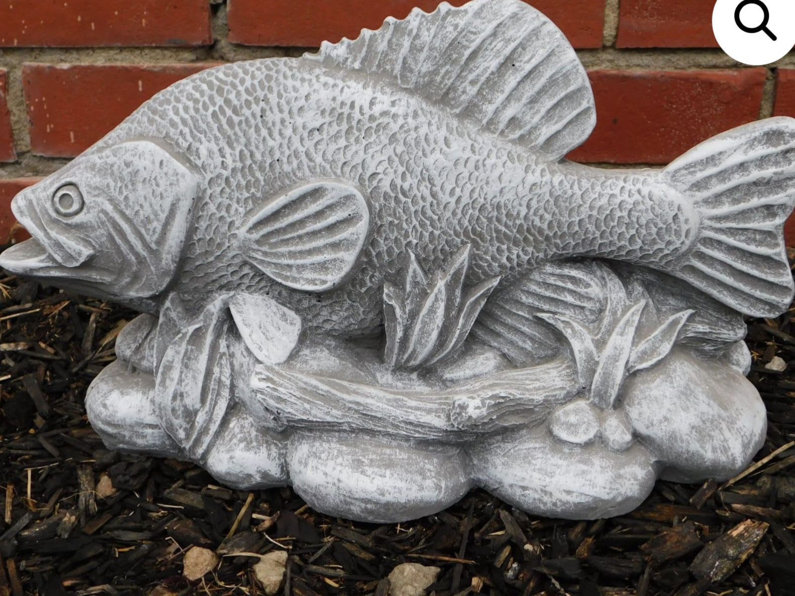 Gray fish garden statue on a brick and mulch background