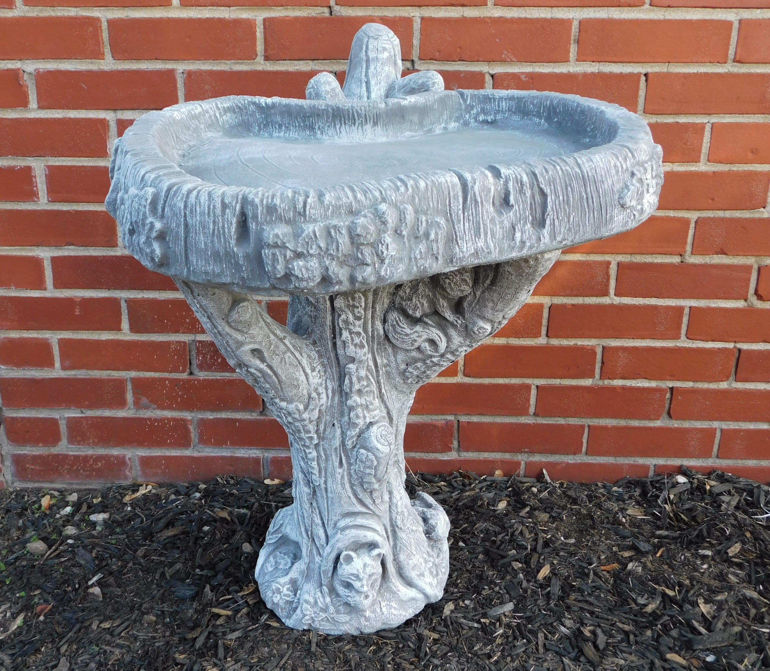 Stone birdbath with an ornate pedestal against a brick wall