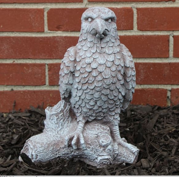 Stone eagle statue on a log in front of a brick wall