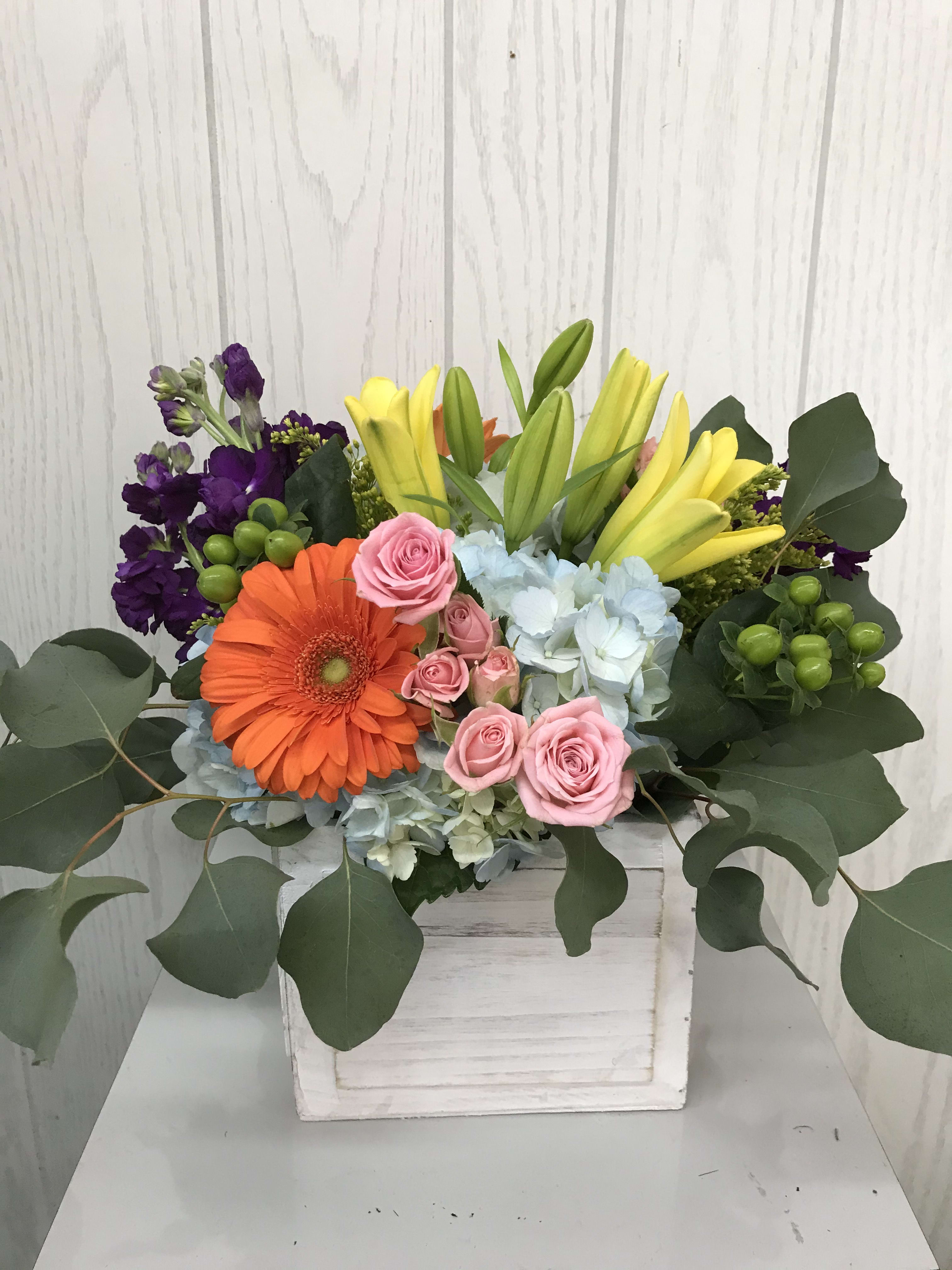 Mixed bouquet in a white wooden box with pink roses, orange gerbera, yellow lilies, and purple blooms