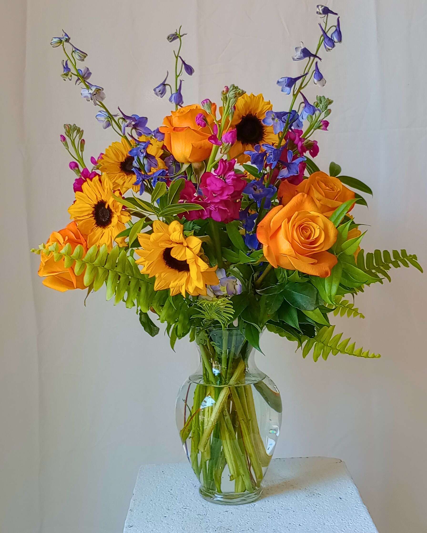 Bouquet of orange roses, sunflowers, and blue flowers in a glass vase