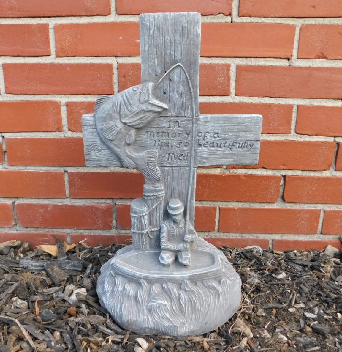 Gray memorial cross sculpture with a fish and kneeling figure