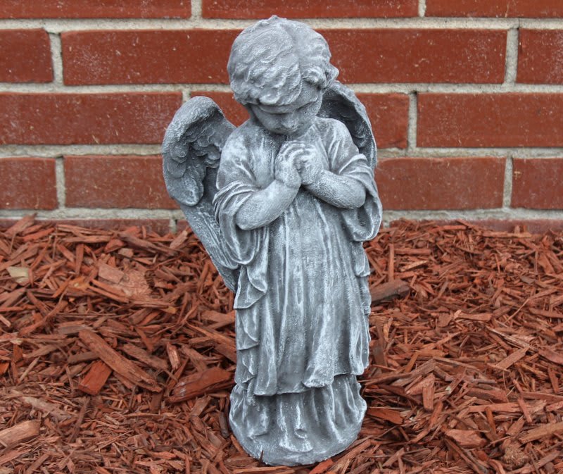 Gray angel statue with folded hands in front of a brick wall