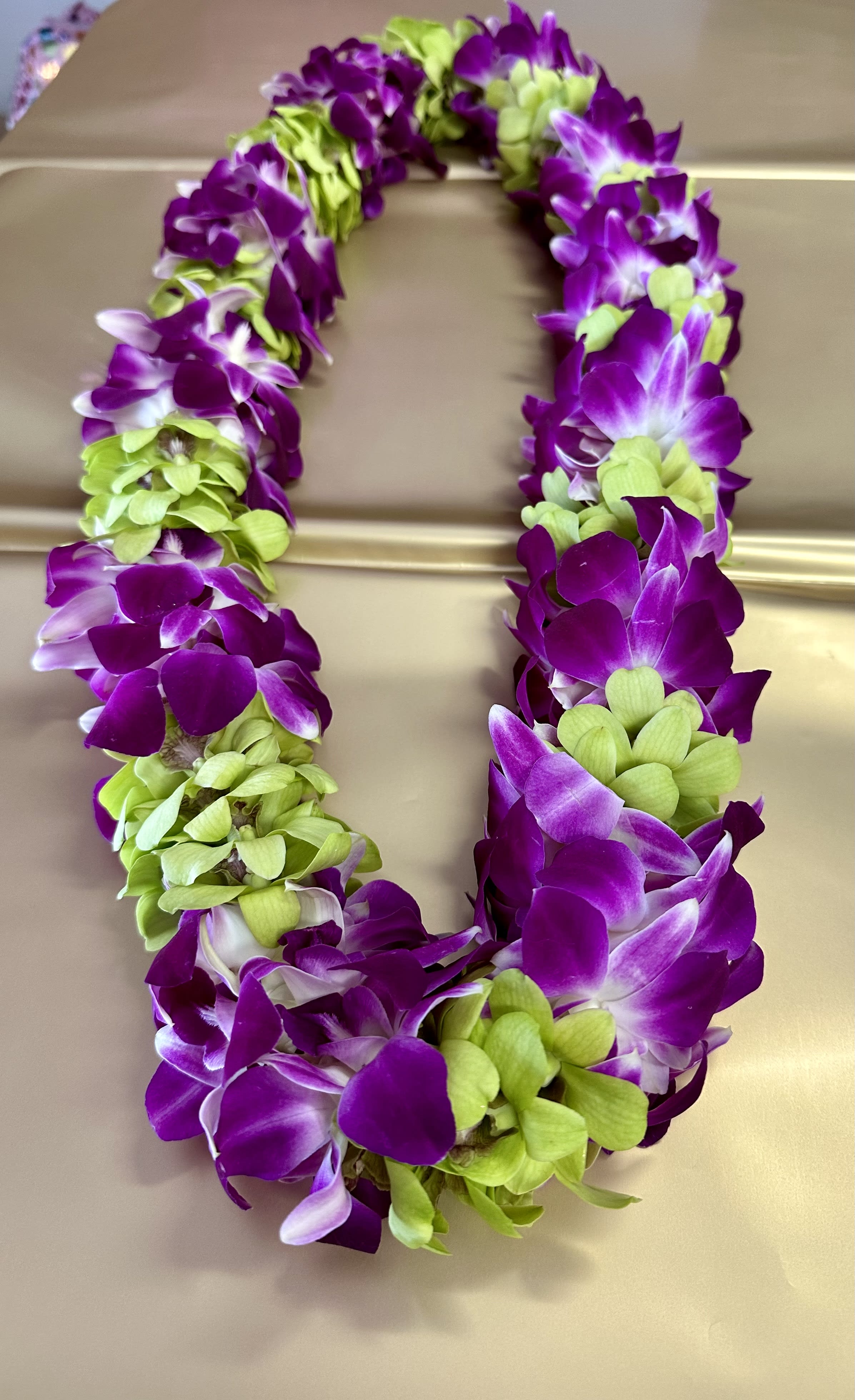 Purple and green orchid lei on a beige surface