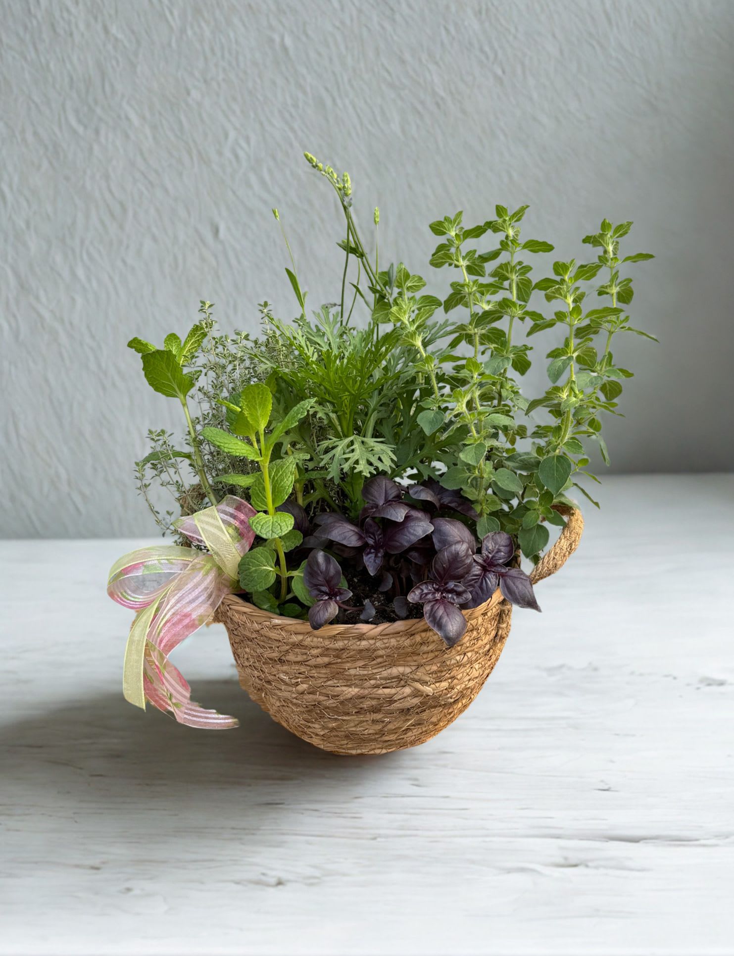 Herb Garden  - Bring fresh flavor and fragrance into any space with this charming herb garden planter. Designed in a natural woven basket and accented with a soft pastel ribbon, this arrangement features a lush mix of culinary herbs such as basil, mint, oregano, and thyme.