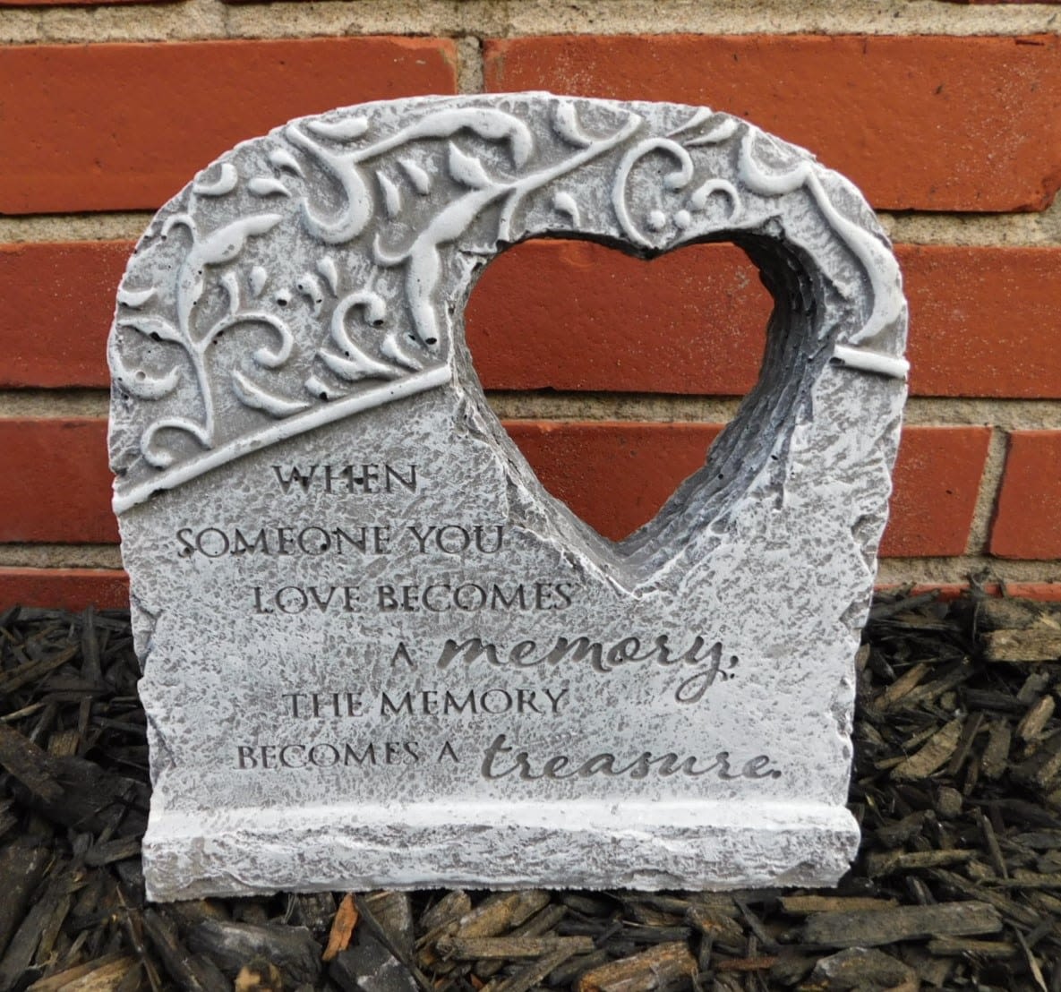 Heart-shaped memorial stone with an engraved quote against a brick wall