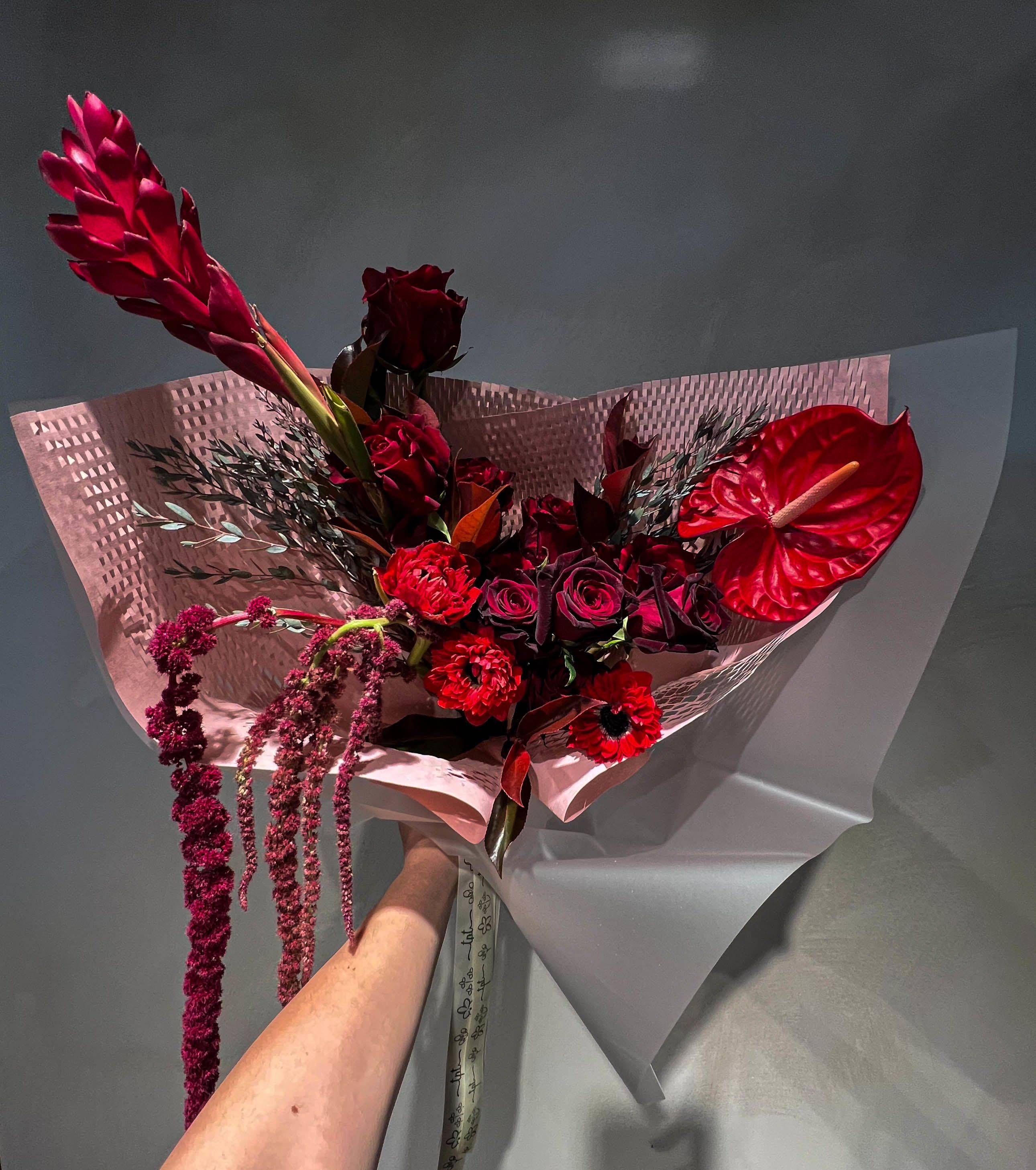 Red bouquet with anthurium, roses, and hanging blooms in pink wrap