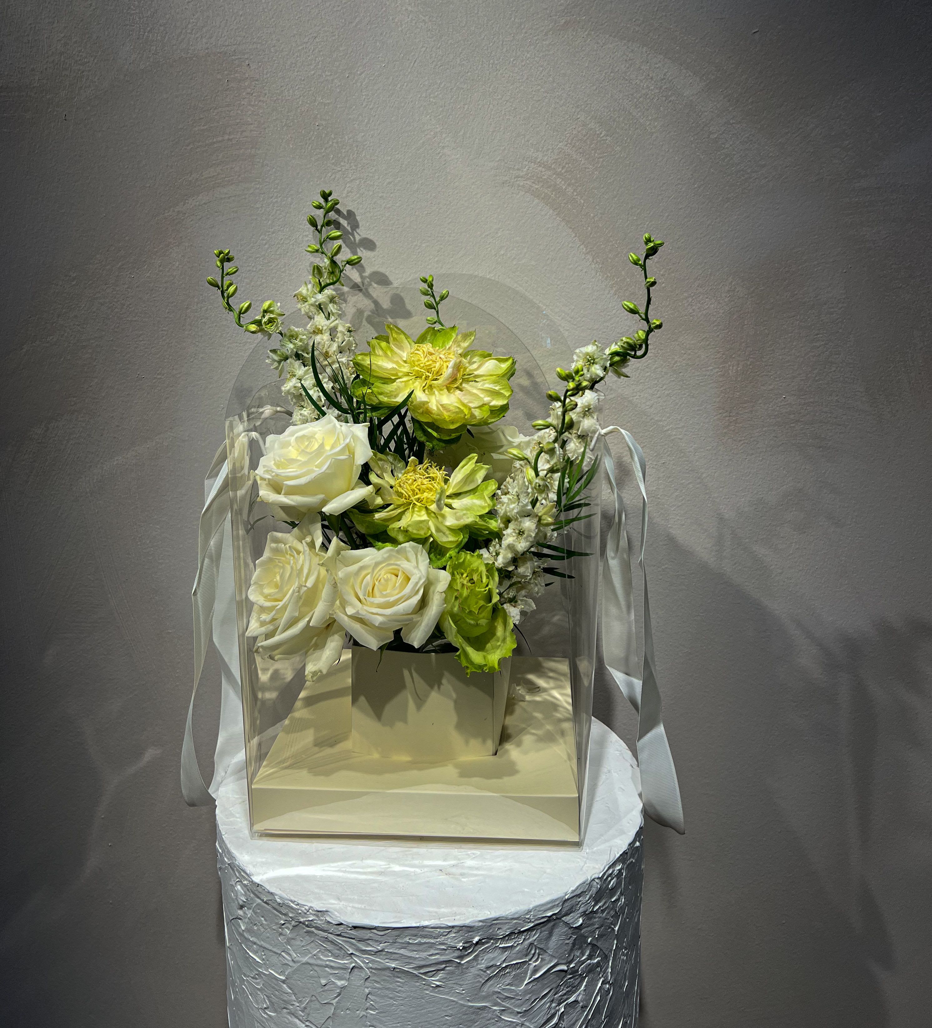 White and lime floral arrangement in a clear box with ribbon handles