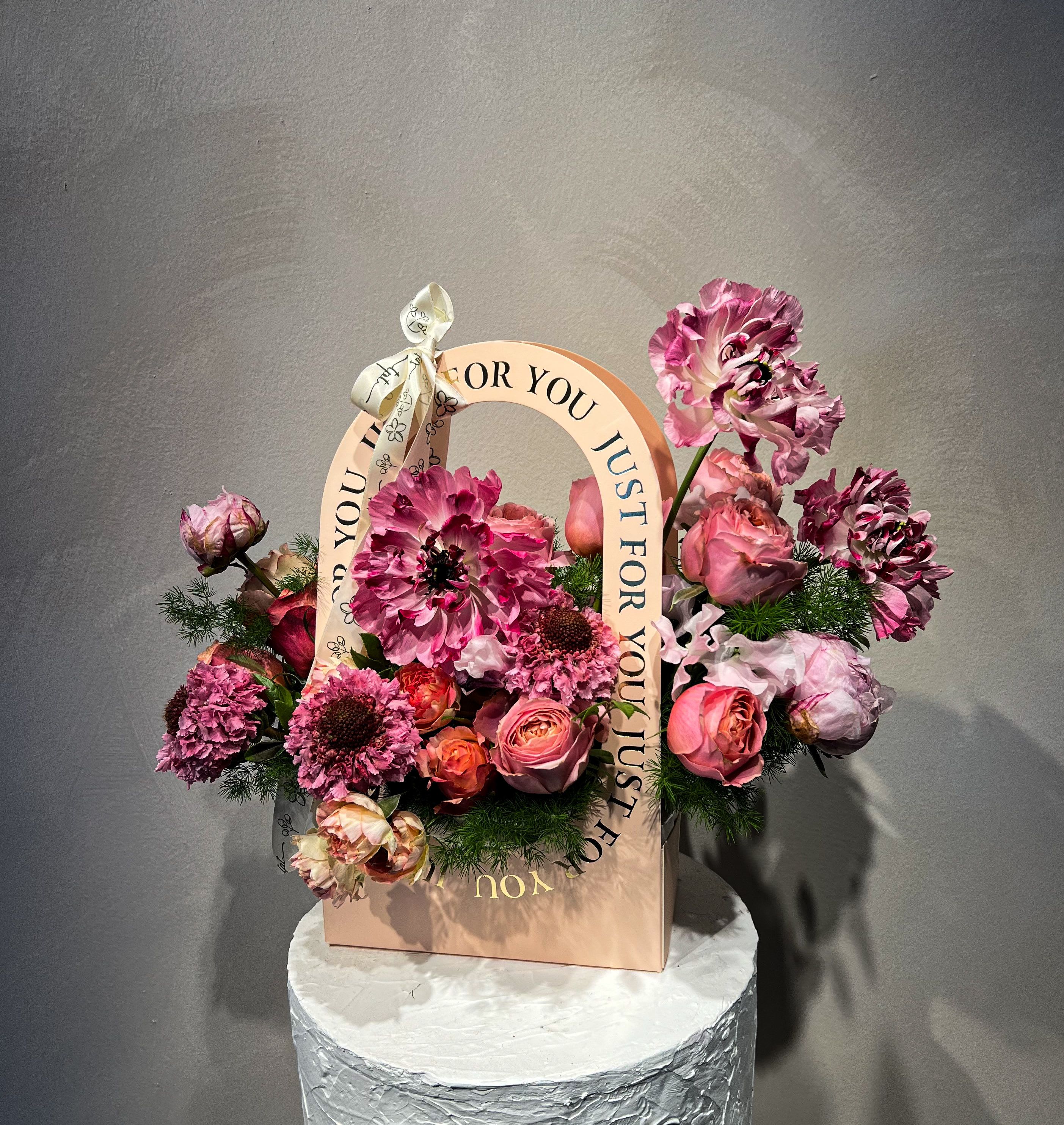 Pink and purple floral arrangement in a gift bag with a ribbon handle