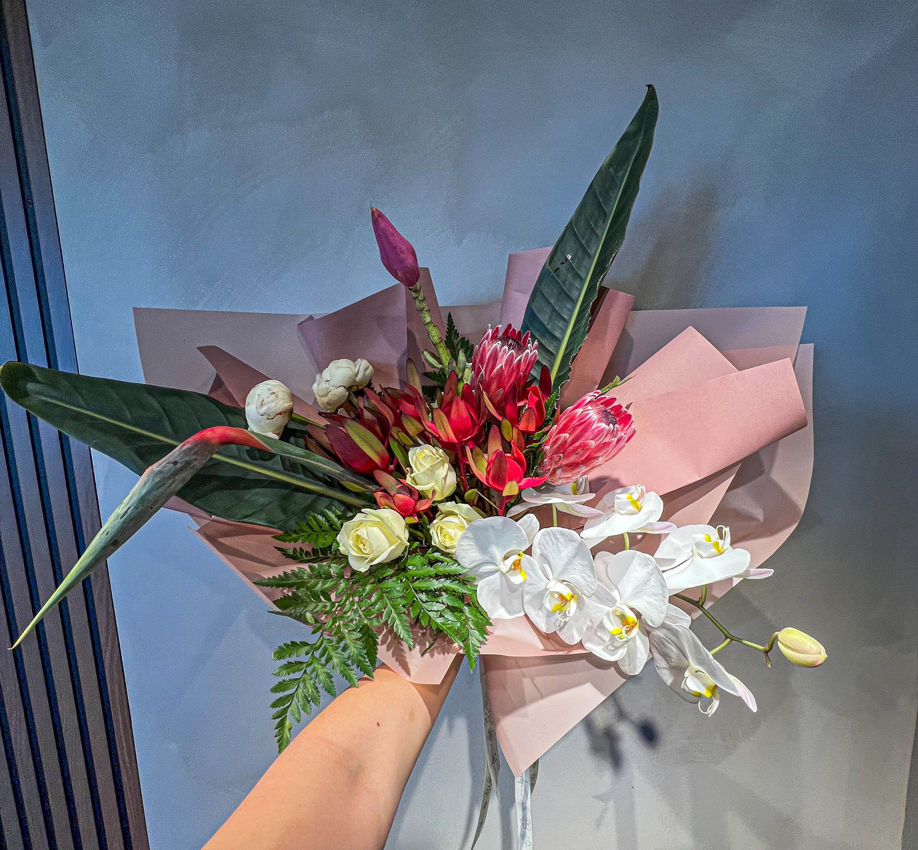 Handheld bouquet with red protea, white orchids, and pink wrapping