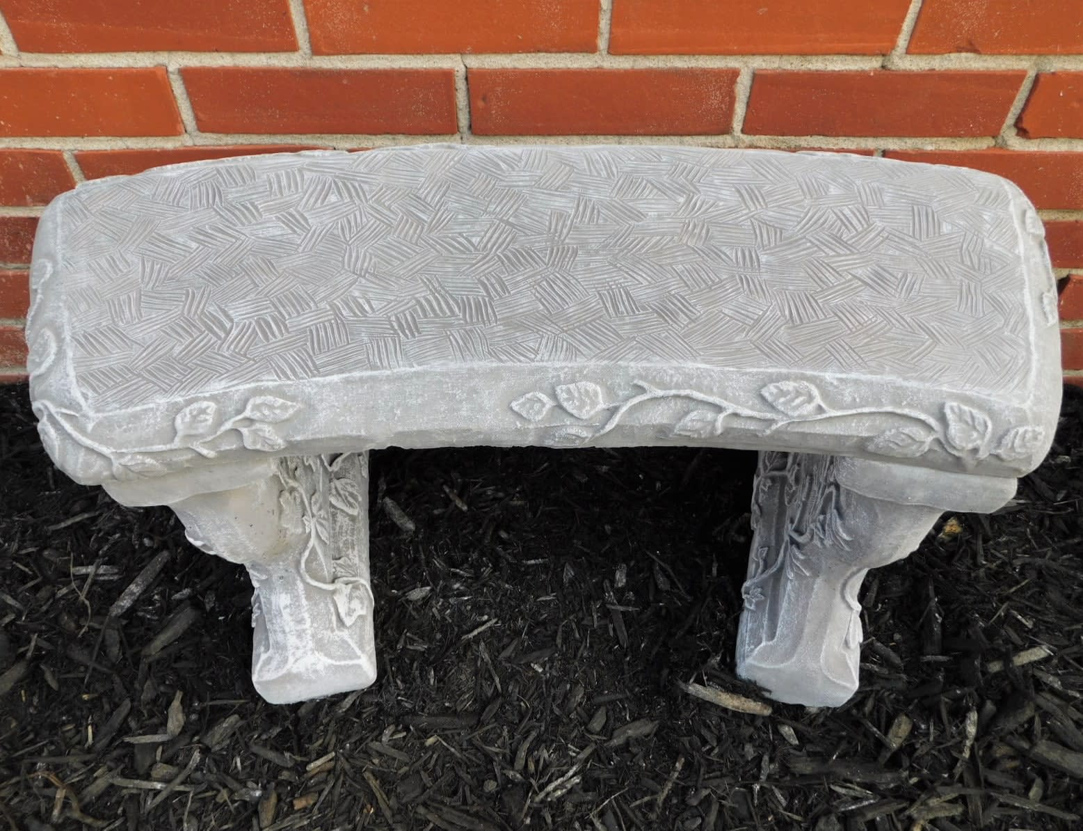 Decorative stone garden bench against a brick wall